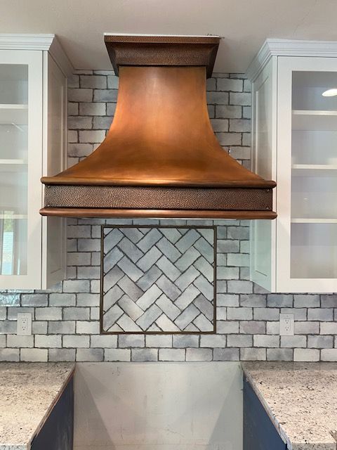 Copper range hood on white subway tile backsplash above a kitchen sink and granite countertops