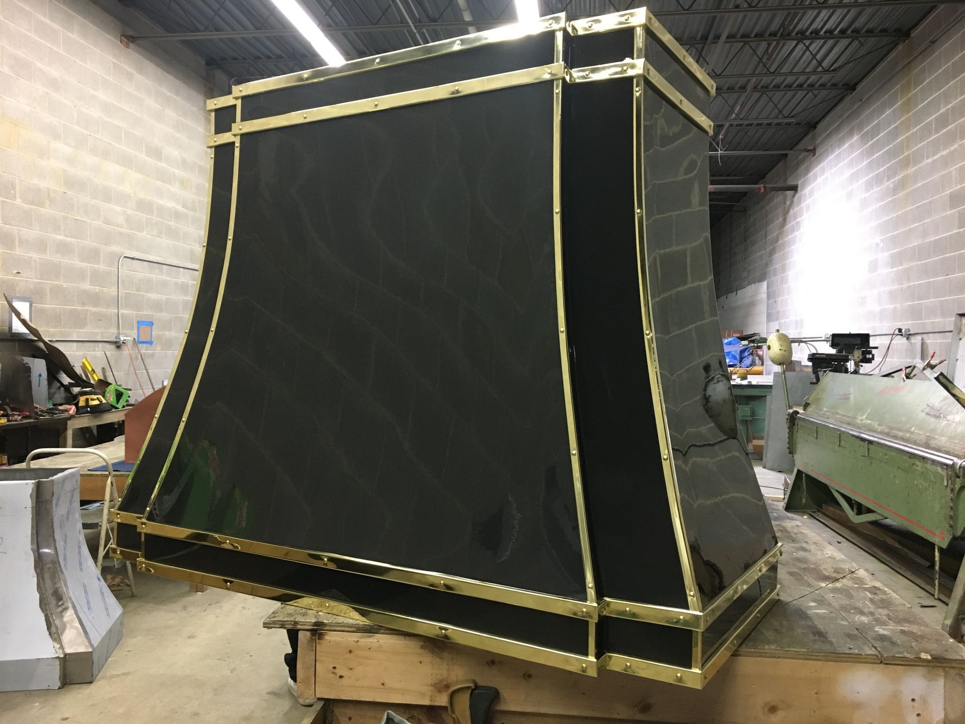 Large black industrial tarp-covered structure in a warehouse, strapped with yellow tape on a wooden pallet.