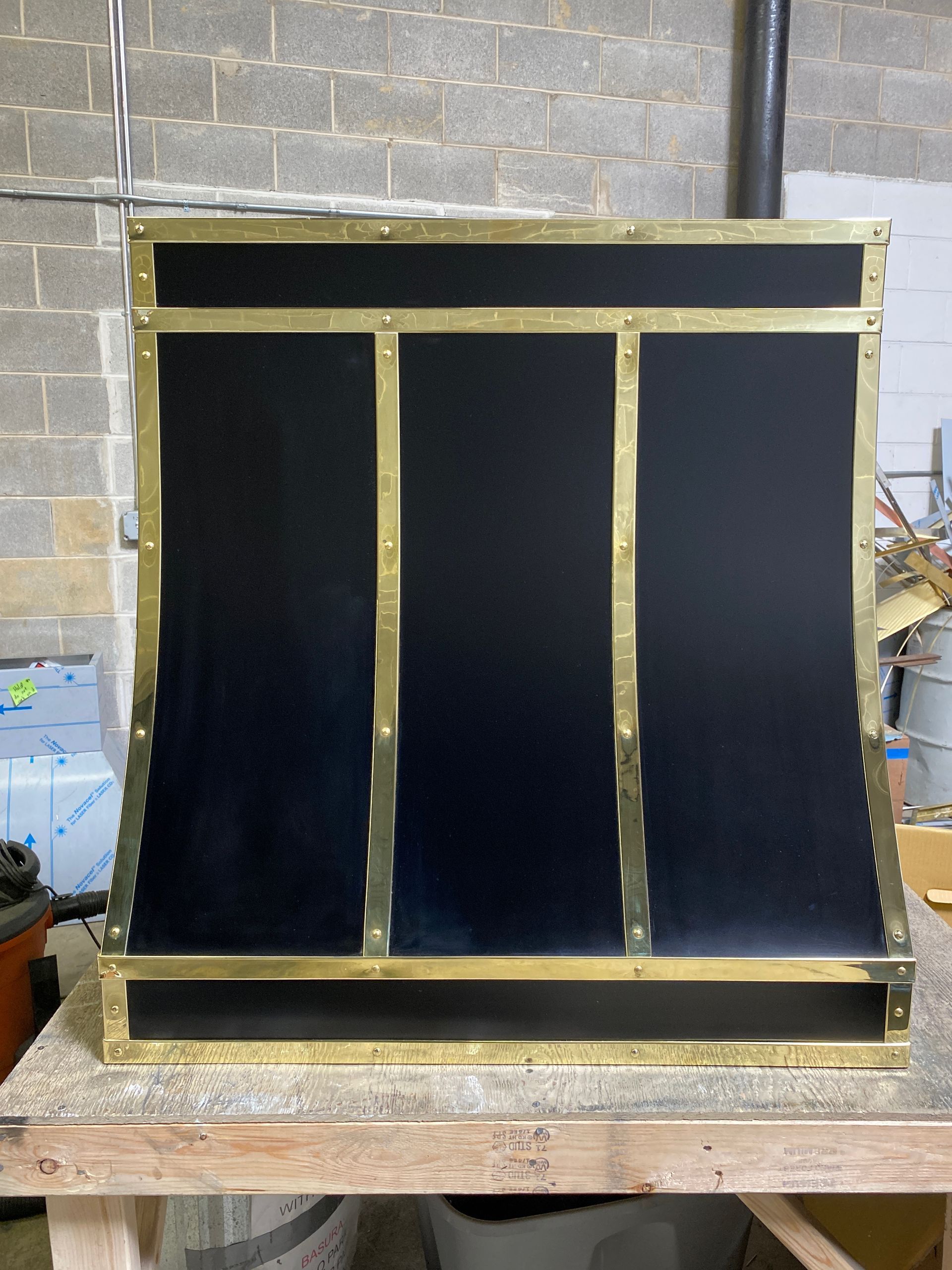 Black three-panel foam board prototype framed in gold tape on a workbench against a brick wall