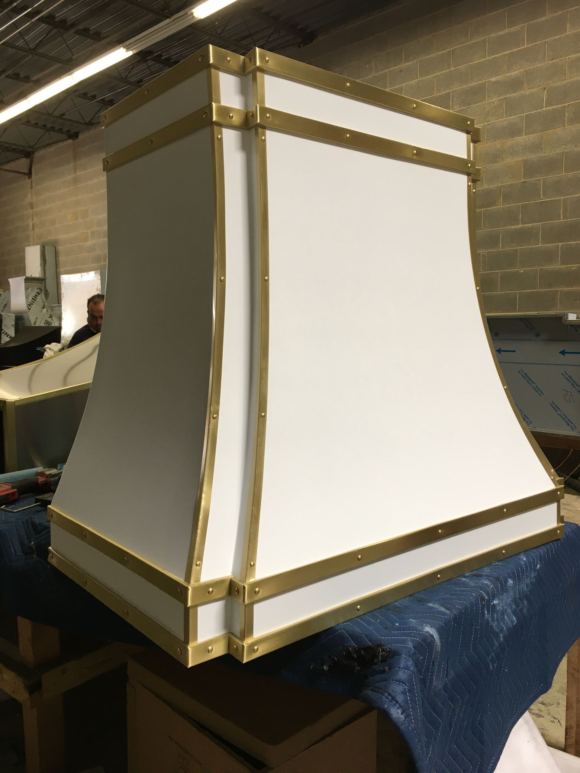 White and gold decorative pedestal with tapered sides on a dark blue cloth in a workshop.