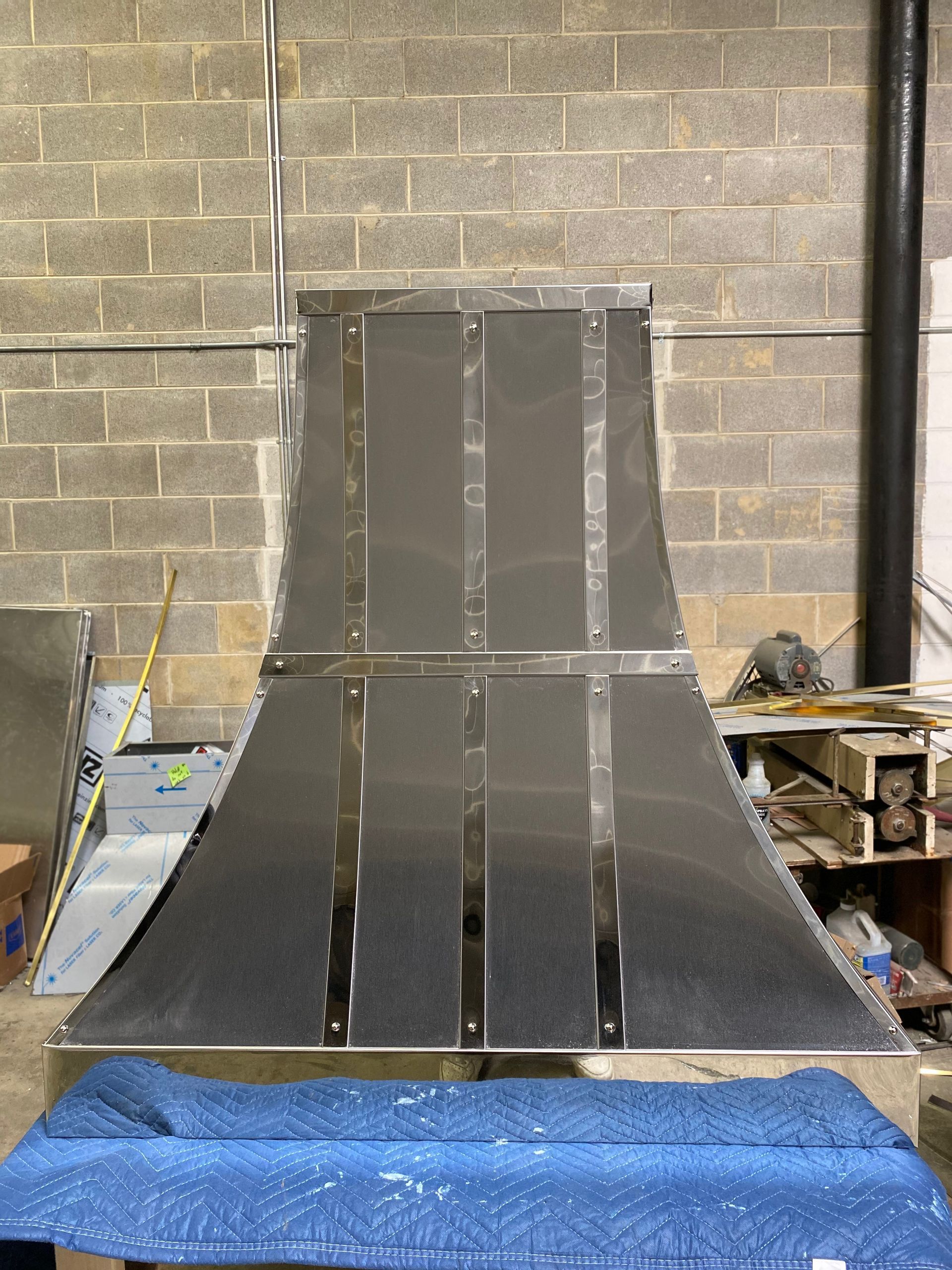 Large gray metal ramp or chute with a raised center panel, set against a cinderblock wall in a workshop.