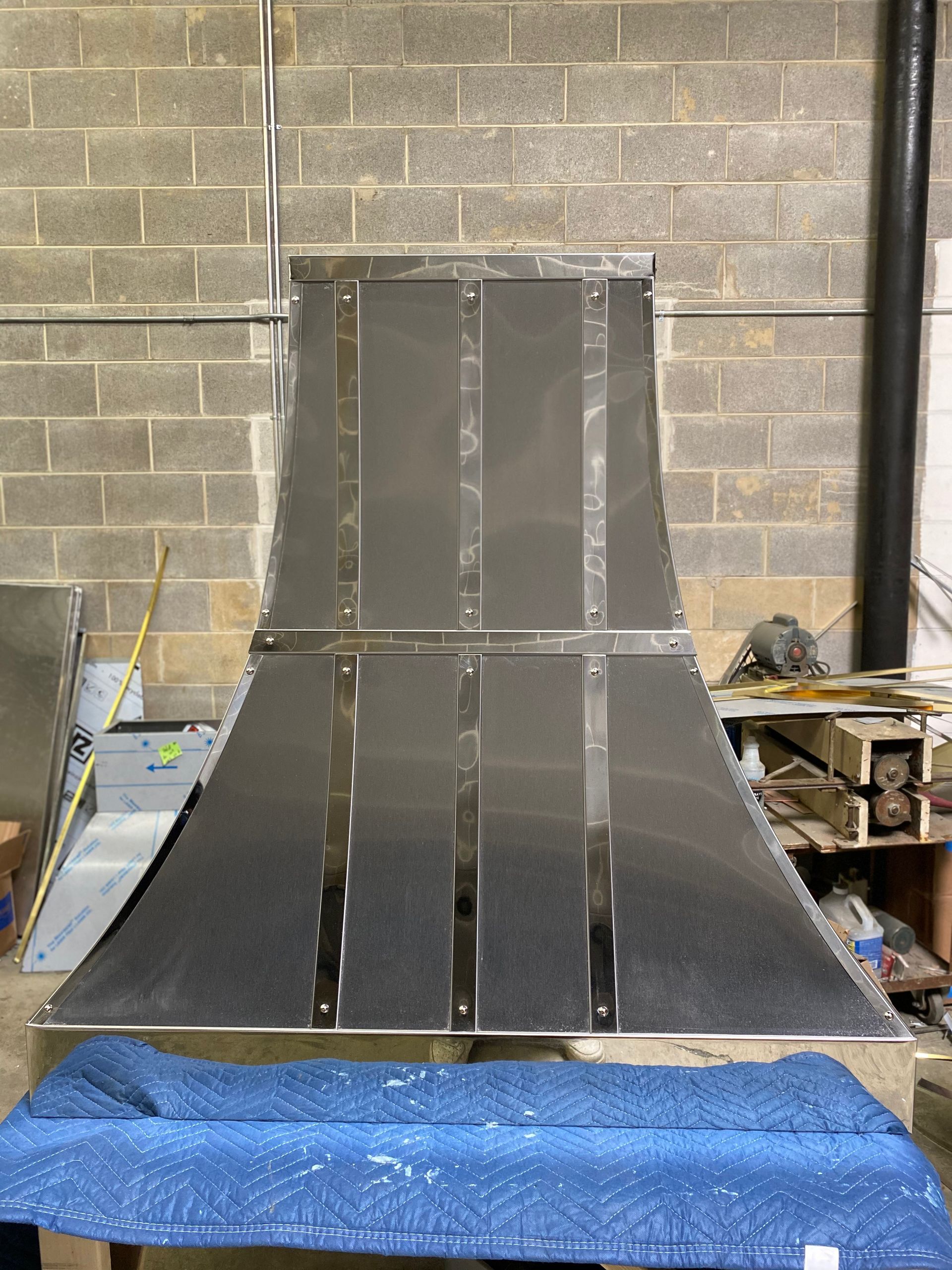 Silver metal ramp prototype in a workshop, with blue padding and cinder block walls behind it