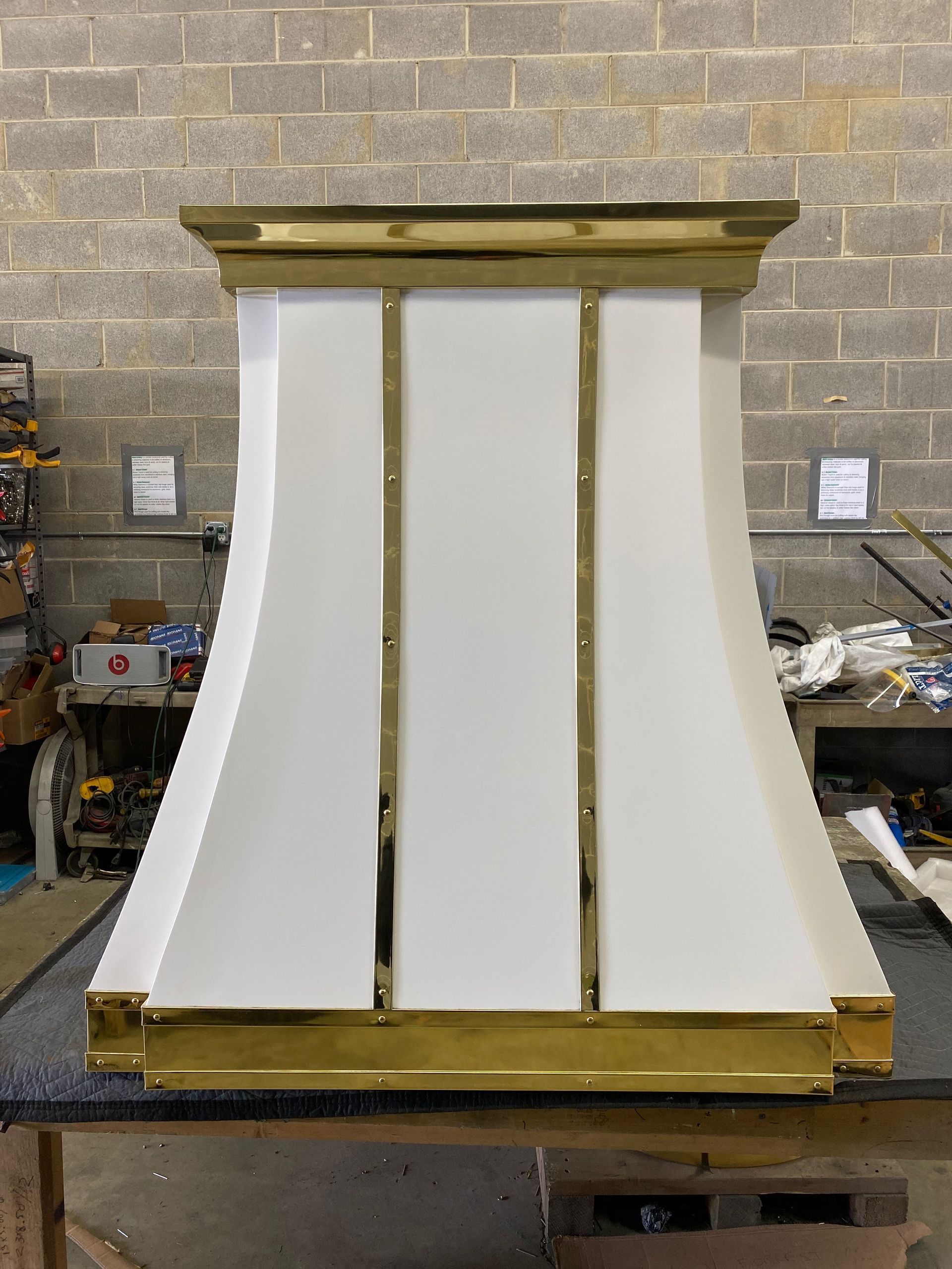 White cabinet/display unit with gold trim on a workbench in a workshop, front view