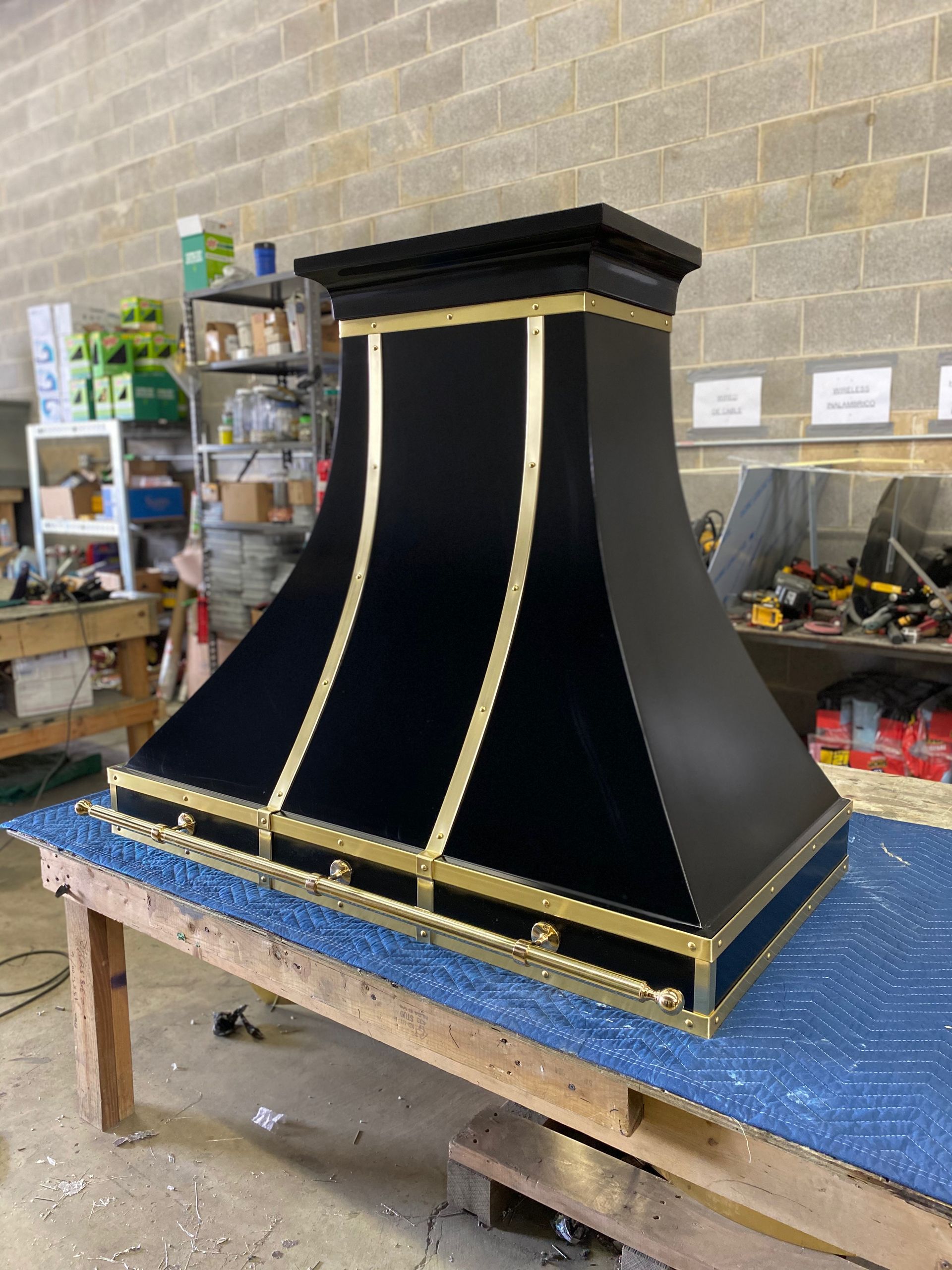 Black decorative mantel or hood with gold trim on a workbench in a workshop