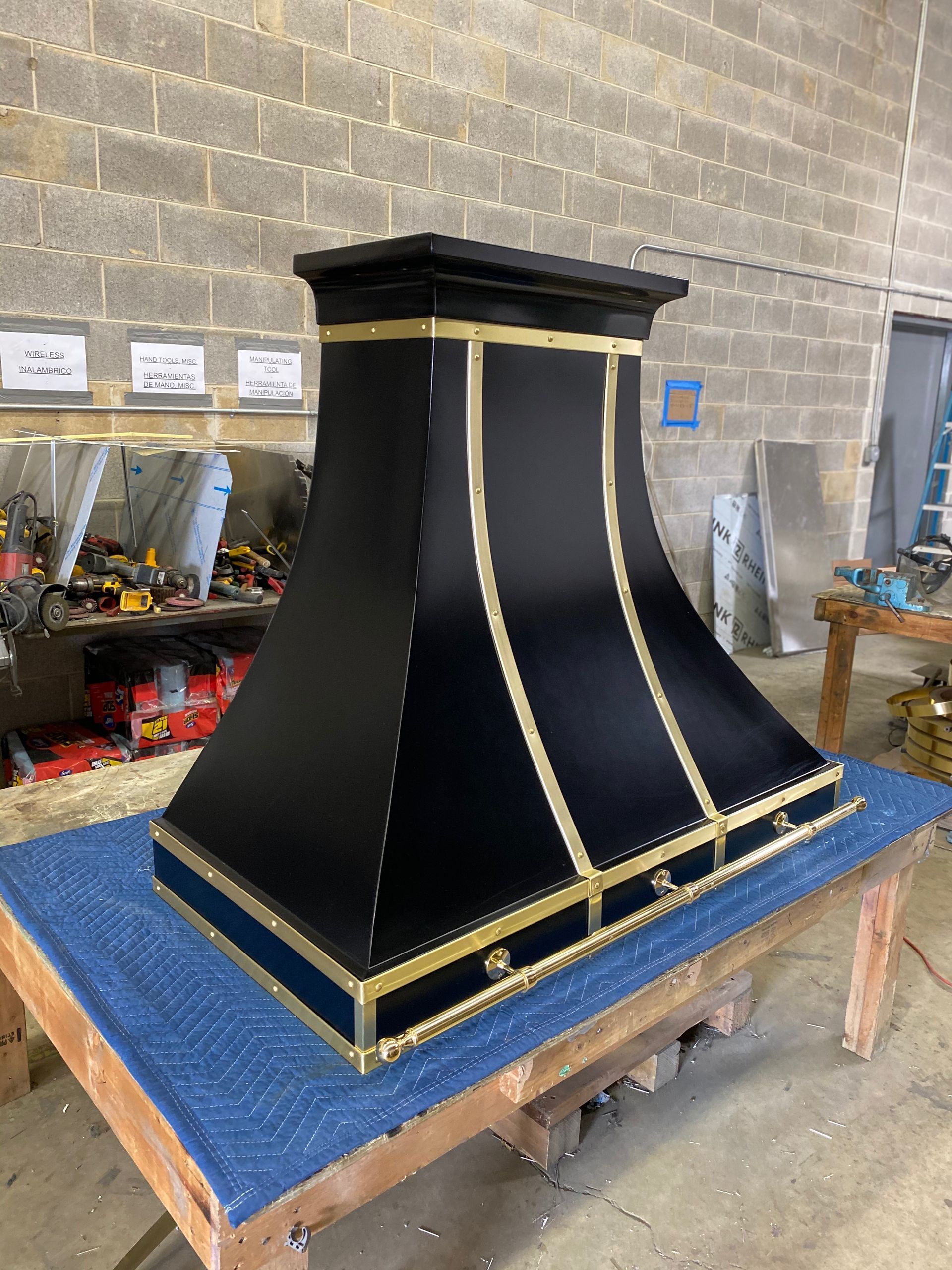 Black decorative chimney hood with gold trim on a workbench in a workshop