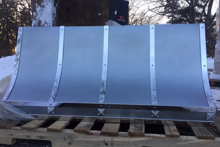 Silver metal snow plow blade mounted on a wooden pallet outdoors in winter.