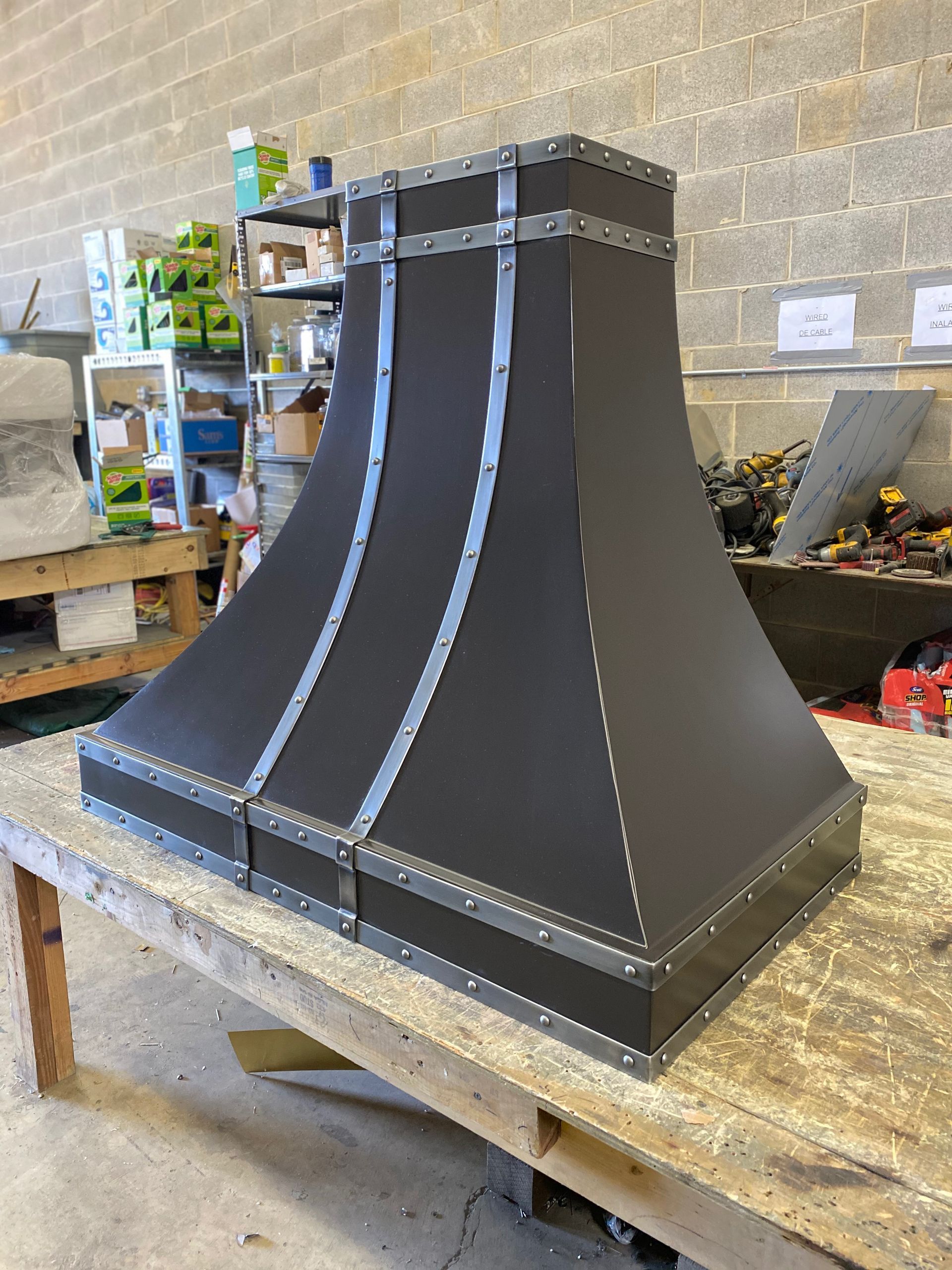 Black tapered metal chimney hood on a workbench in a workshop