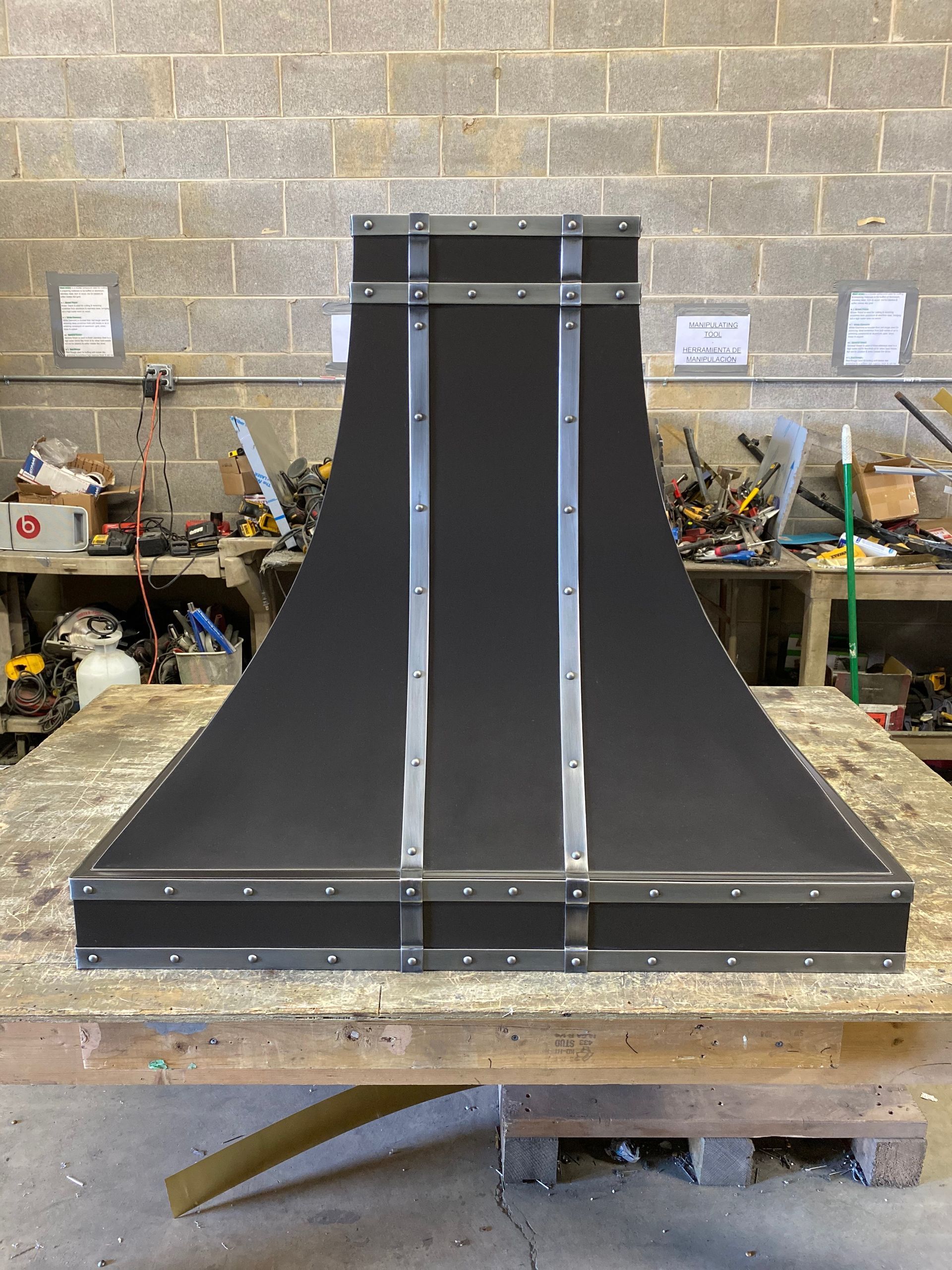 Black metal funnel-shaped structure on a workbench in a workshop, with silver support strips.