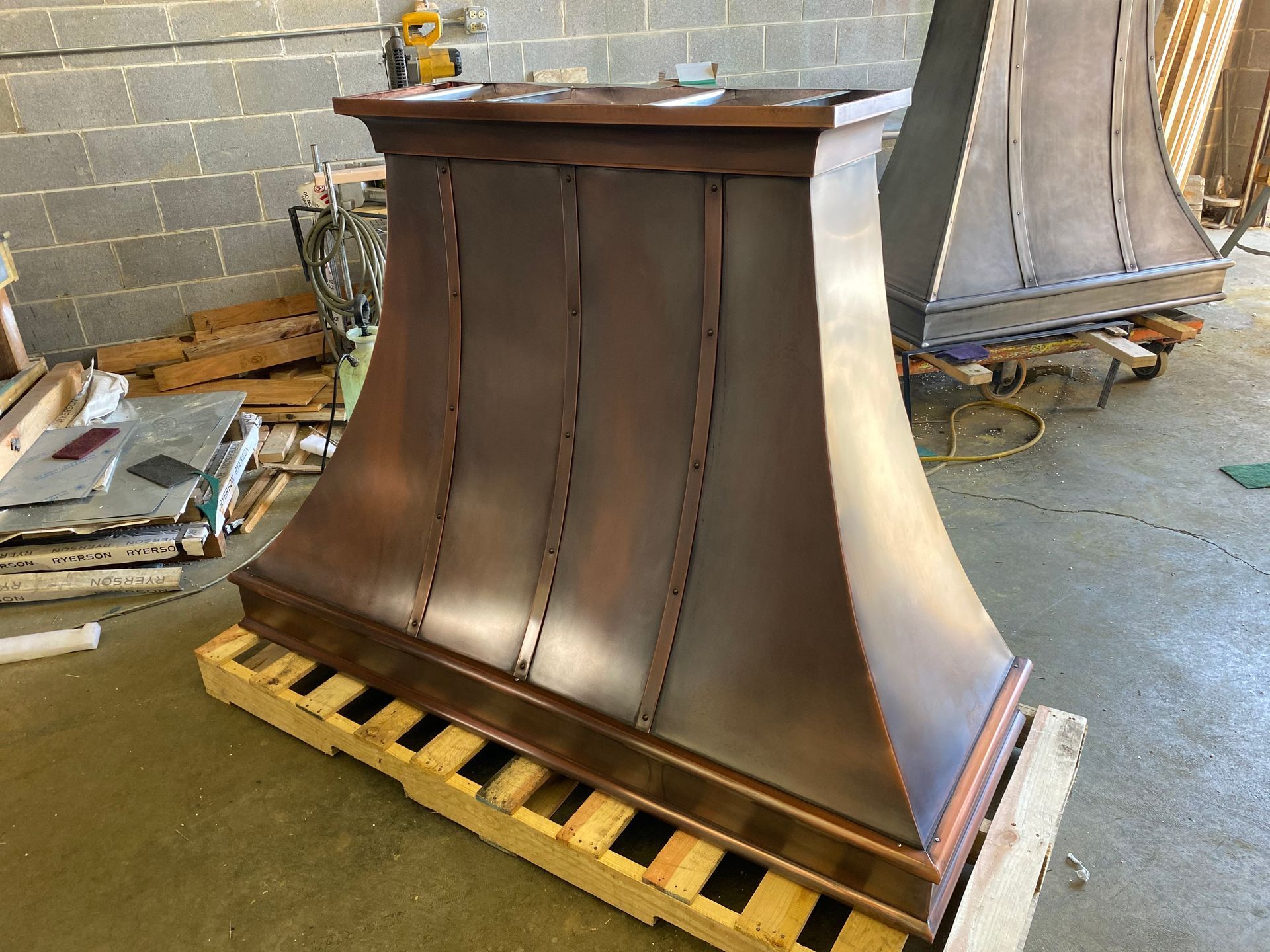 Large copper-colored metal pedestal or base on a wooden pallet in a workshop.