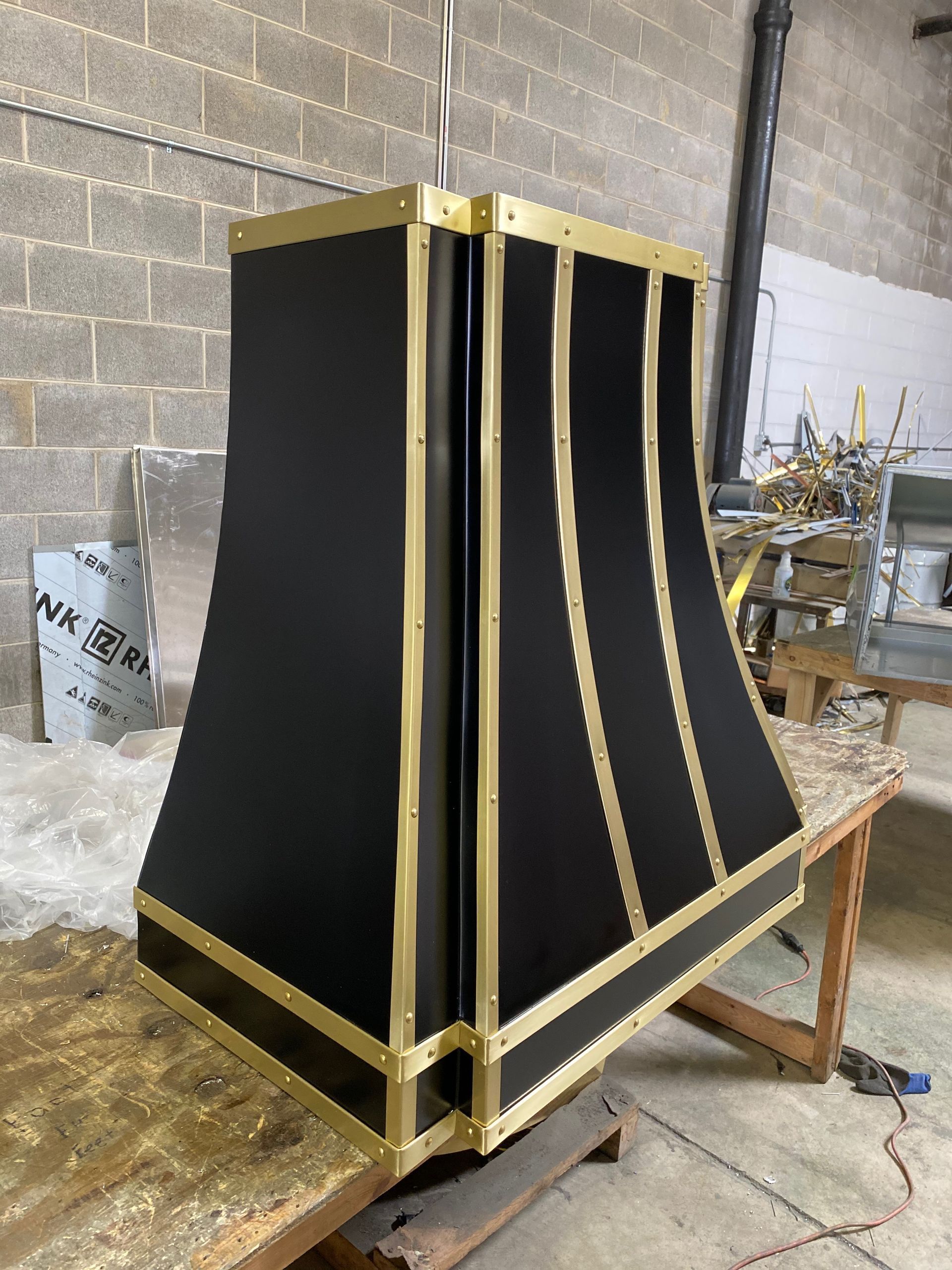Black-and-gold decorative panel structure in a workshop, angled on a workbench against a brick wall.
