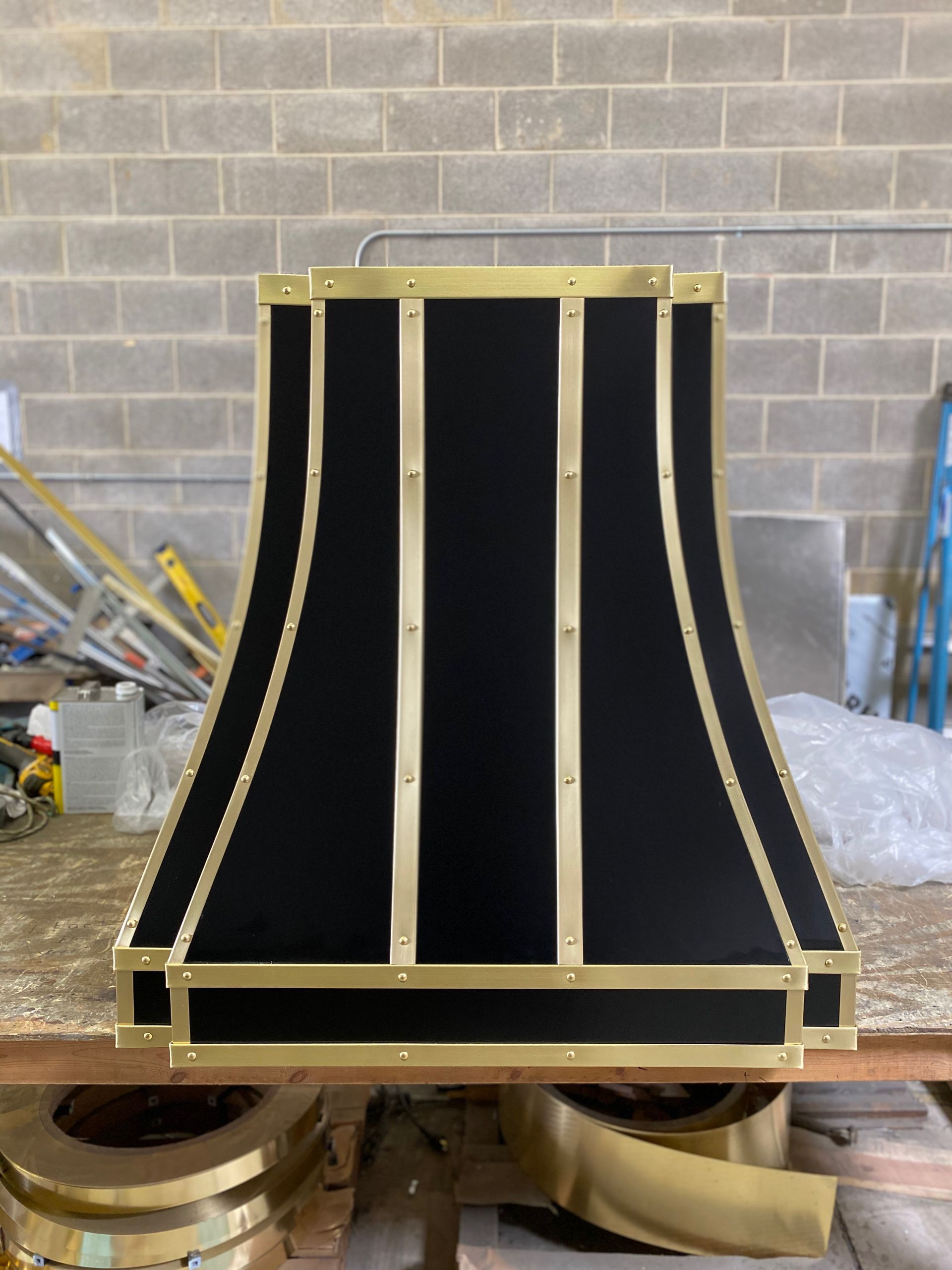 Black curved panel framed in wood, standing on a workshop floor against a brick wall.