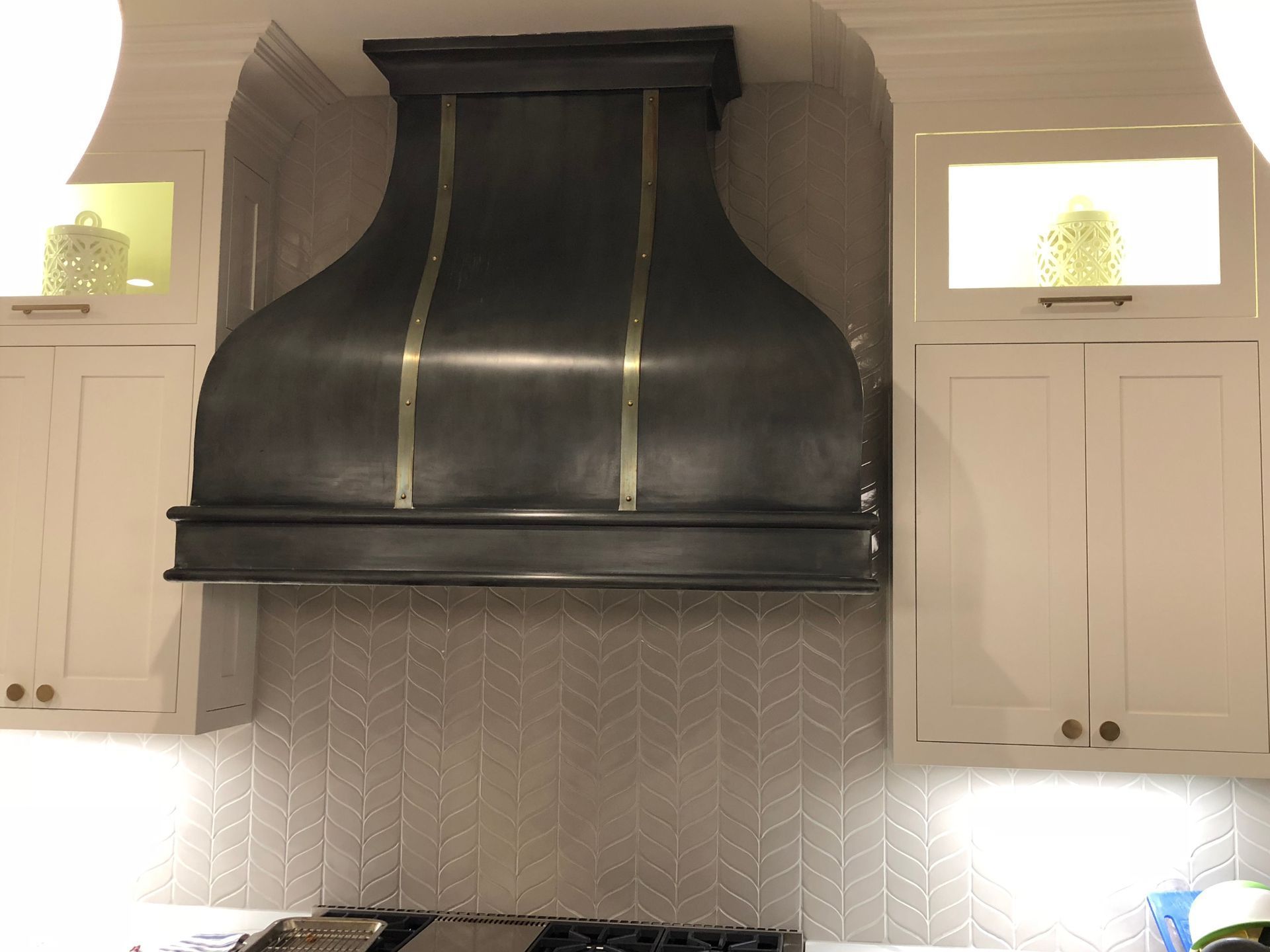 Black kitchen range hood between white cabinets with a silver tile backsplash