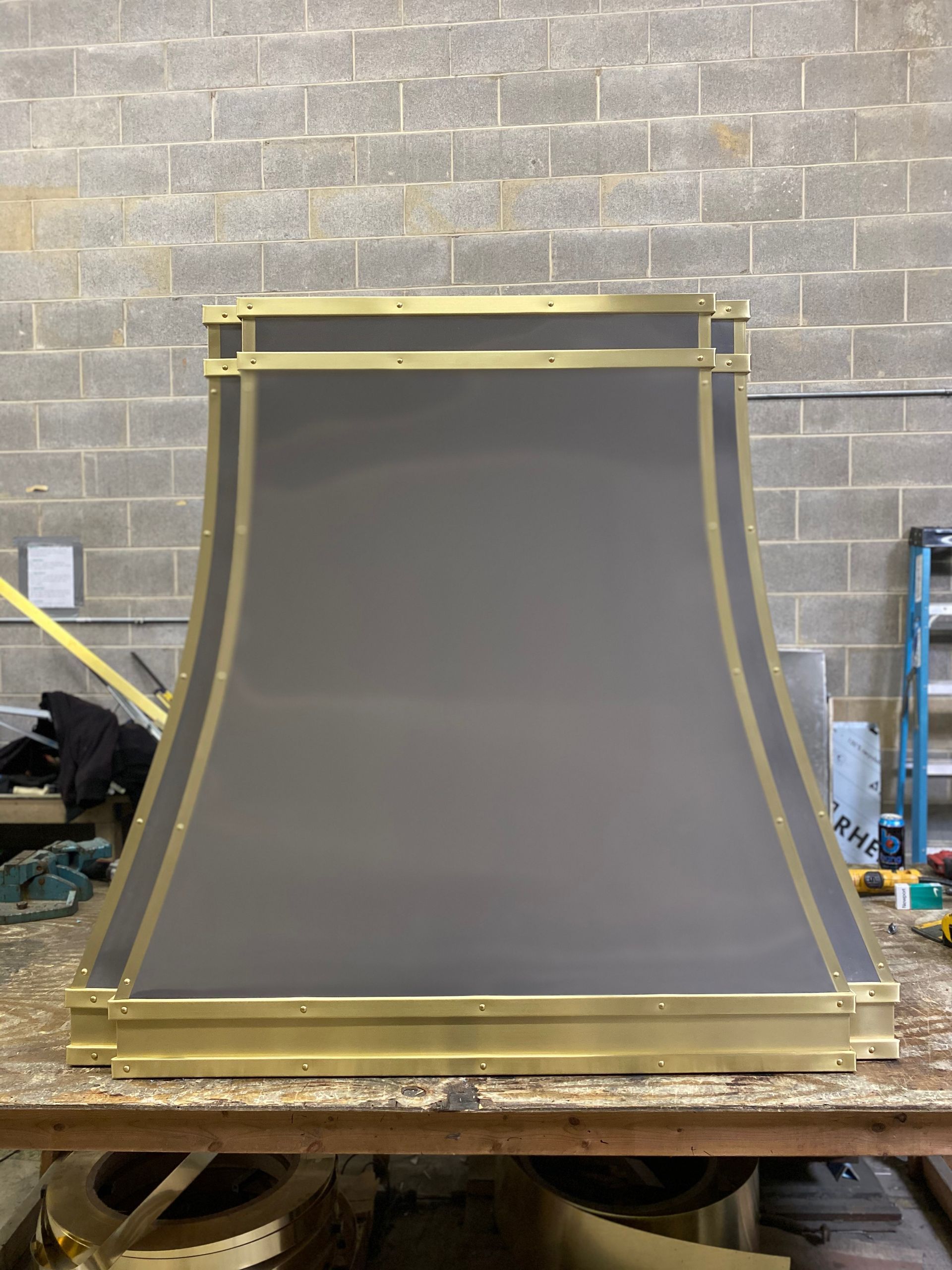 Large gray metal panel with gold trim leaning on a workbench in an industrial workshop