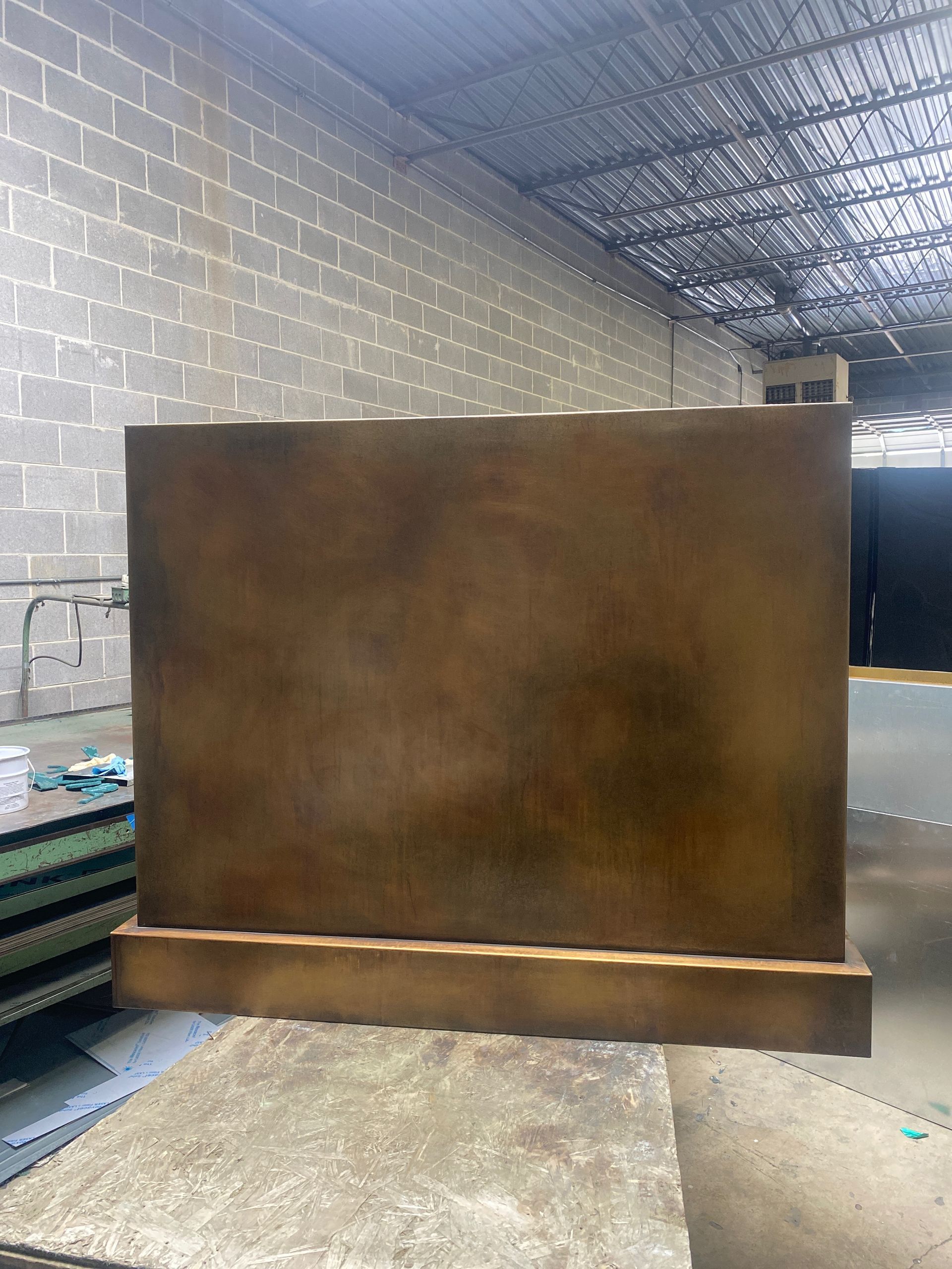 Large rust-colored metal panel leaning in an industrial warehouse aisle