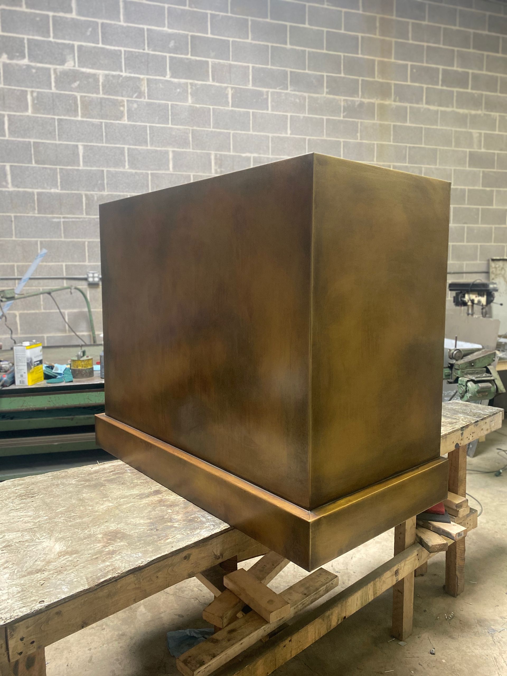 Large rust-colored metal box on a workbench in an industrial workshop, with a cinderblock wall behind it