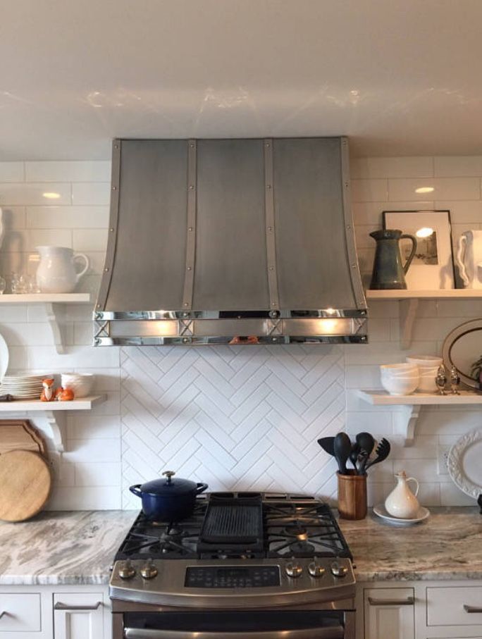 Modern kitchen with gray range hood, white tile backsplash, and stove with cookware and utensils