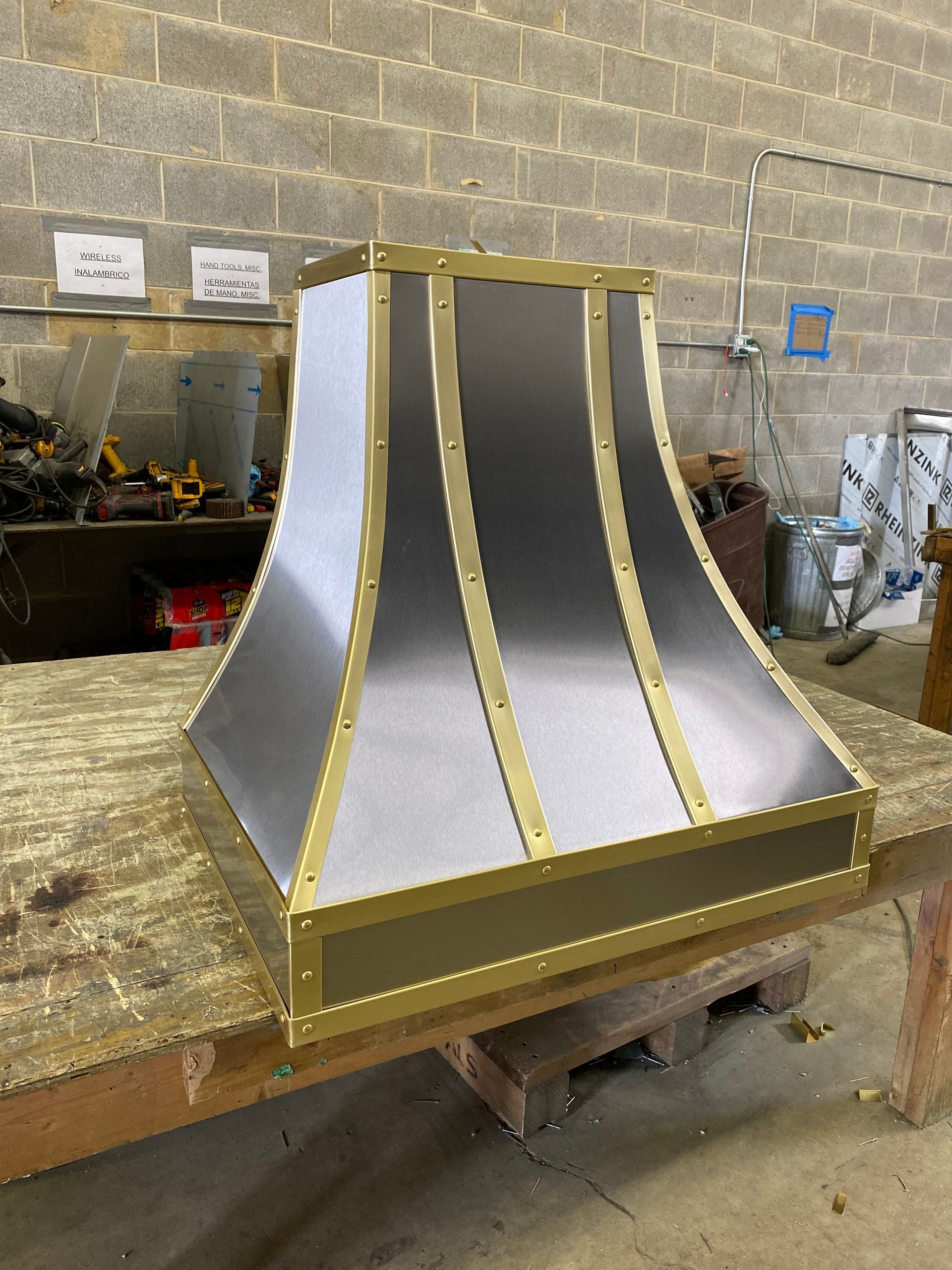 Metallic curved architectural model on a workbench in a workshop, with silver panels and gold trim.