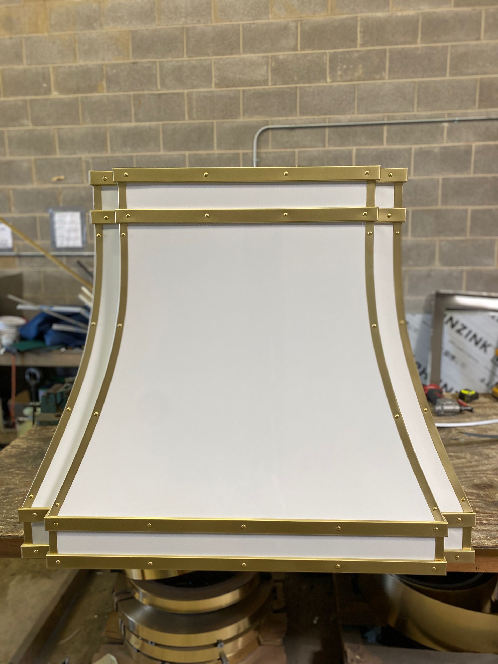 White lampshade with gold trim on a workbench in a workshop against a brick wall