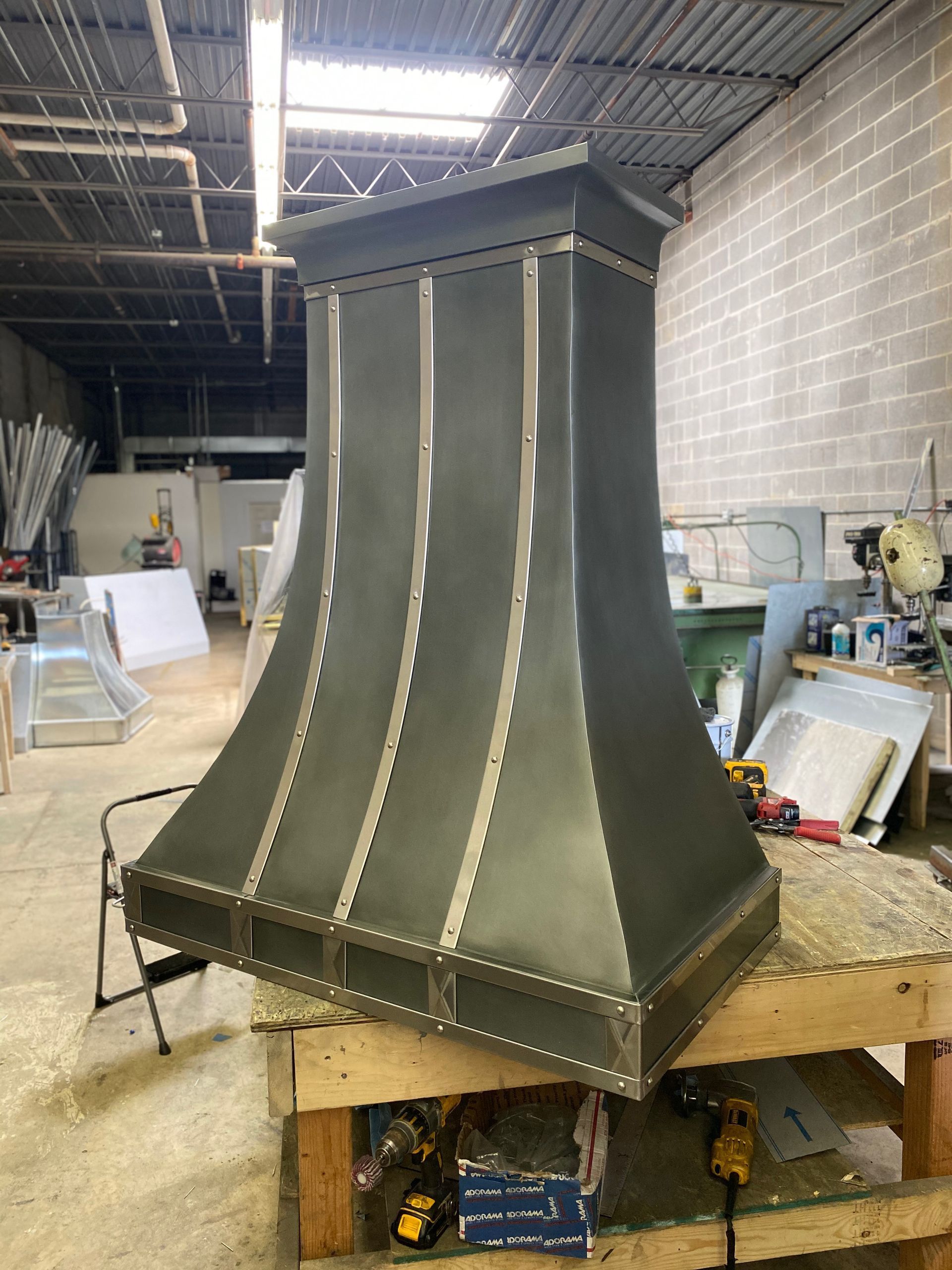 Large black metal hood or chimney cover in a workshop, sitting on a workbench.