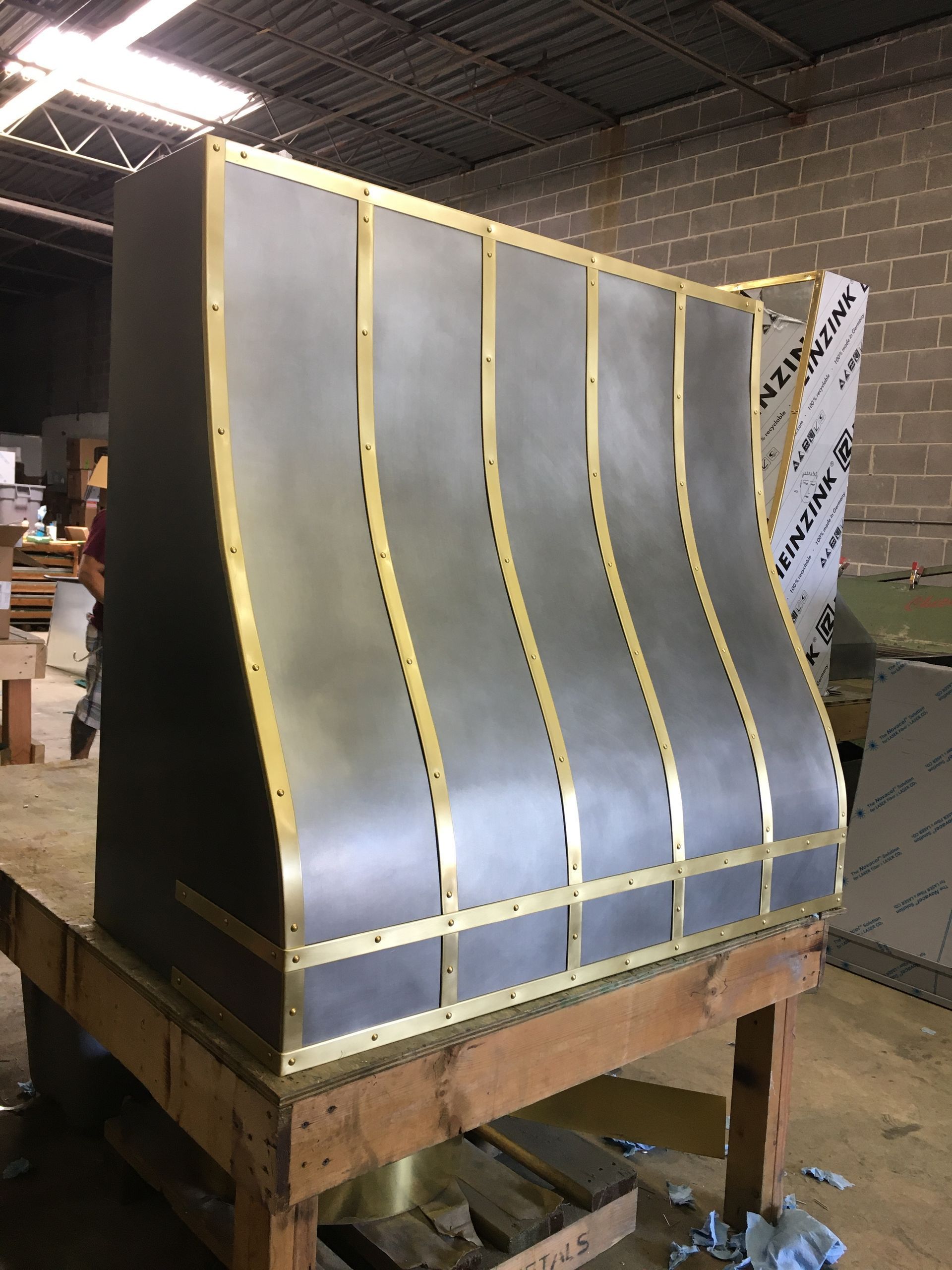 Curved metal panel with gold trim on a wooden pallet in an industrial warehouse