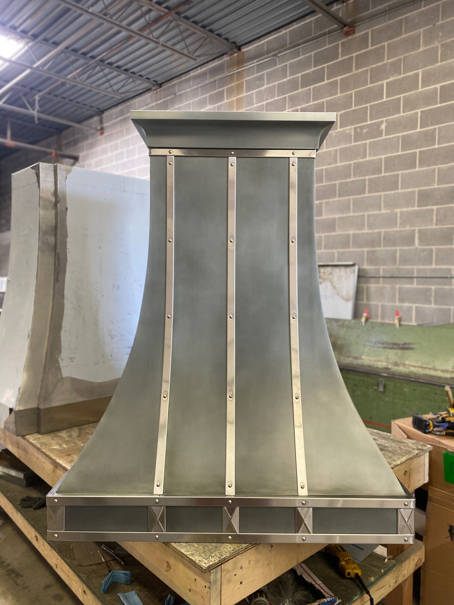 Large metal industrial duct or hood assembly in a warehouse, with curved panels and a flat top.
