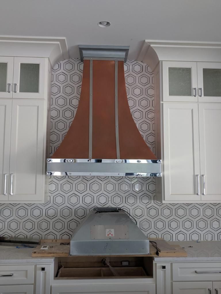 Modern kitchen with white cabinets, patterned backsplash, and a copper range hood above a stovetop