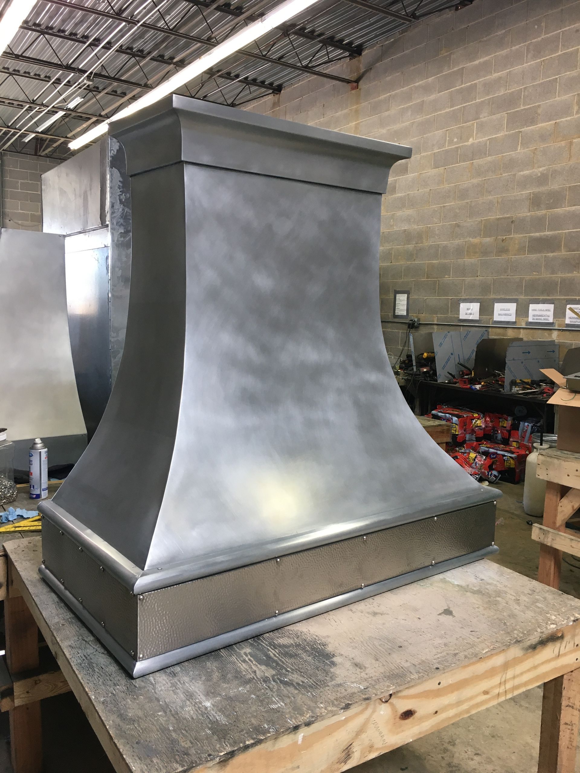 Large gray metal hood or chimney on a workbench in an industrial workshop.
