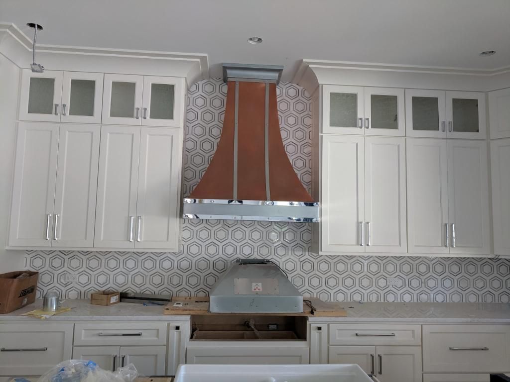 White kitchen with patterned backsplash, white cabinets, and a copper range hood above the stove.