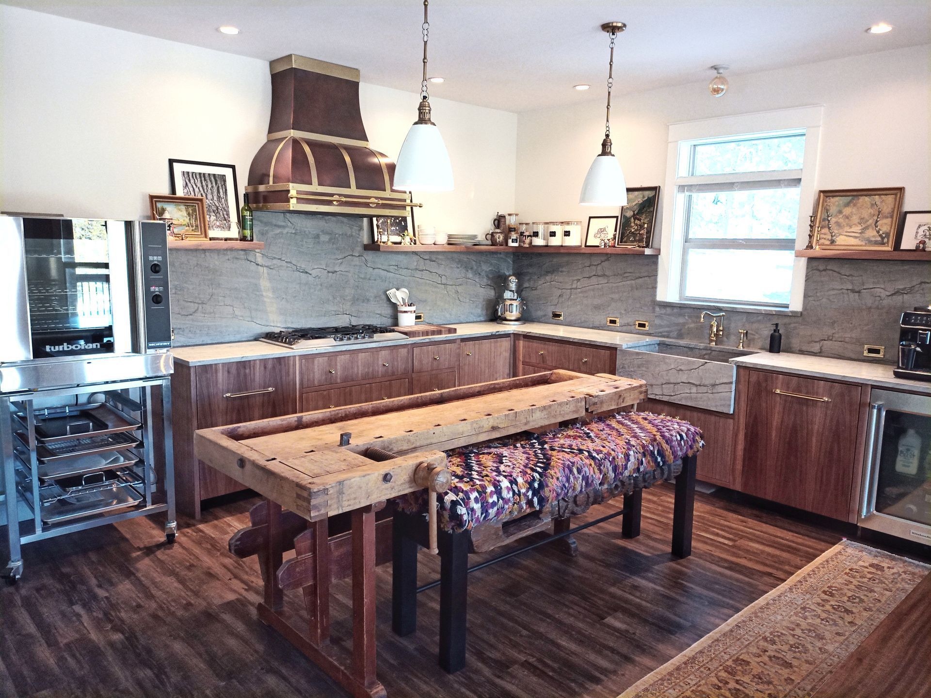 Rustic kitchen with wood cabinets, dark countertops, and a large wooden dining table center stage