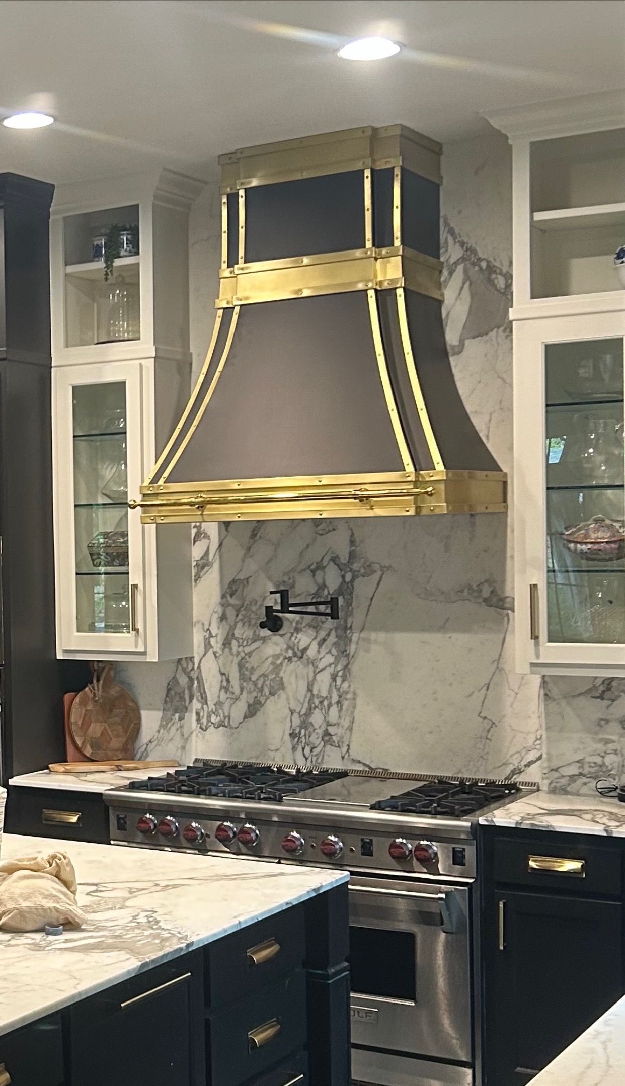 Modern kitchen with navy cabinets, marble countertops, and a gold range hood over a stove.
