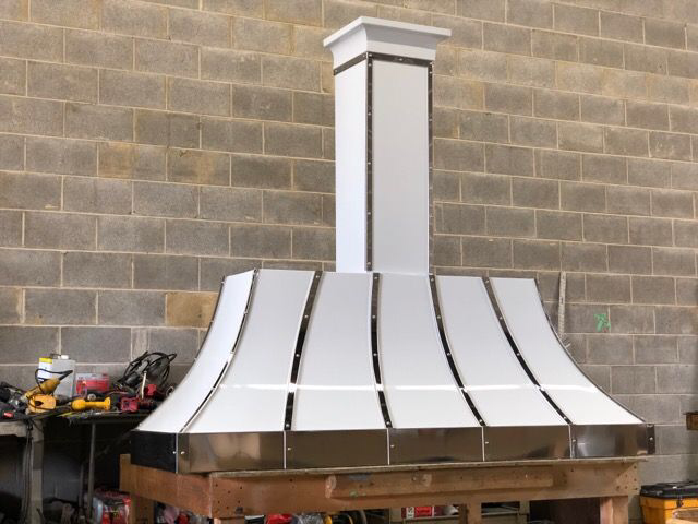 White metal chimney hood against a tan brick wall, with tools on a workbench to the left