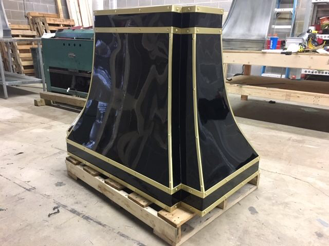 Black glossy decorative column base with gold trim on a wooden pallet in a workshop.
