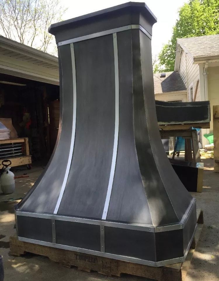 Black metal chimney hood on a workbench outdoors with a gray roof and vertical silver trim