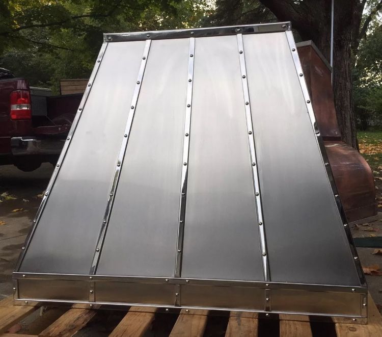 Shiny metal roof panel leaning on a wooden pallet outdoors under trees