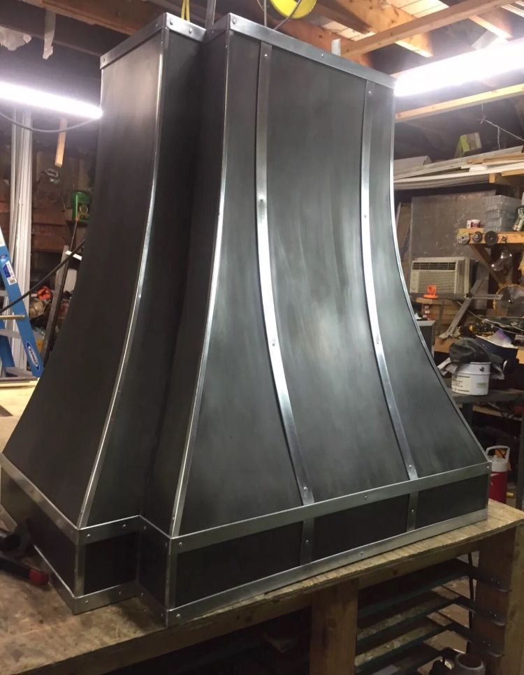 Large black metal ventilation hood in a workshop, with curved sides and silver trim.