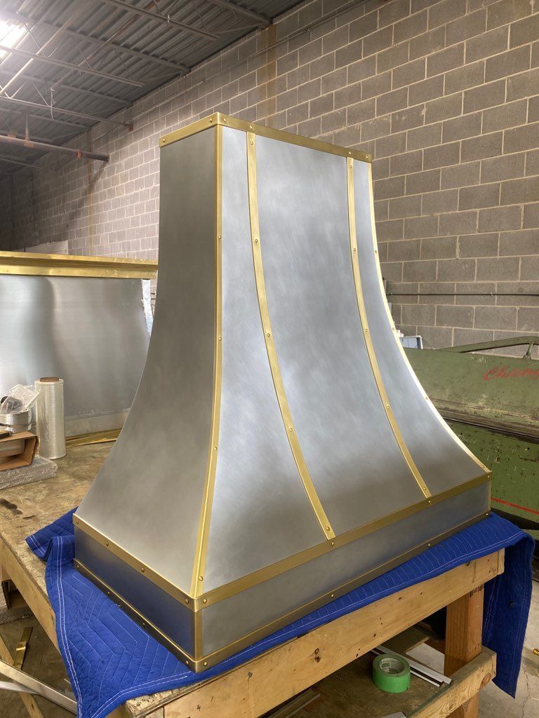 Metal duct hood with silver panels and gold trim on a blue-covered workbench in a workshop