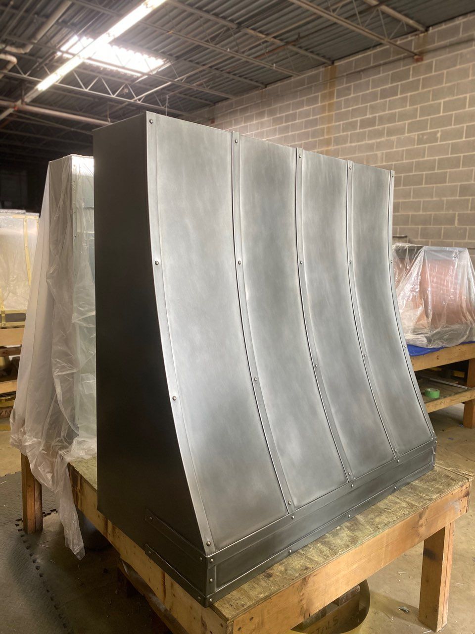 Large curved metal duct panel on a wooden workbench in an industrial workshop