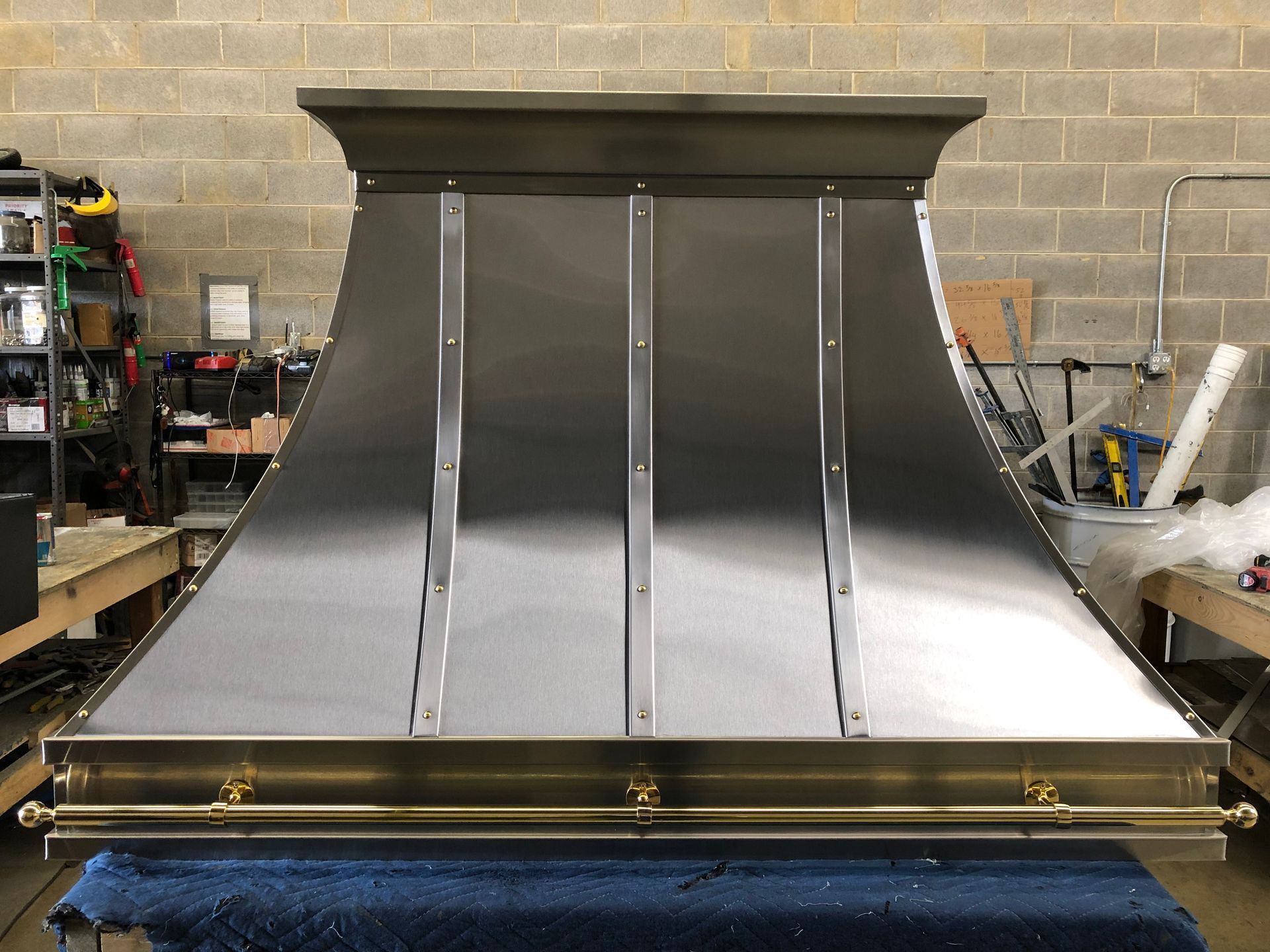 Large metal ventilation hood with polished panels in a workshop against a brick wall