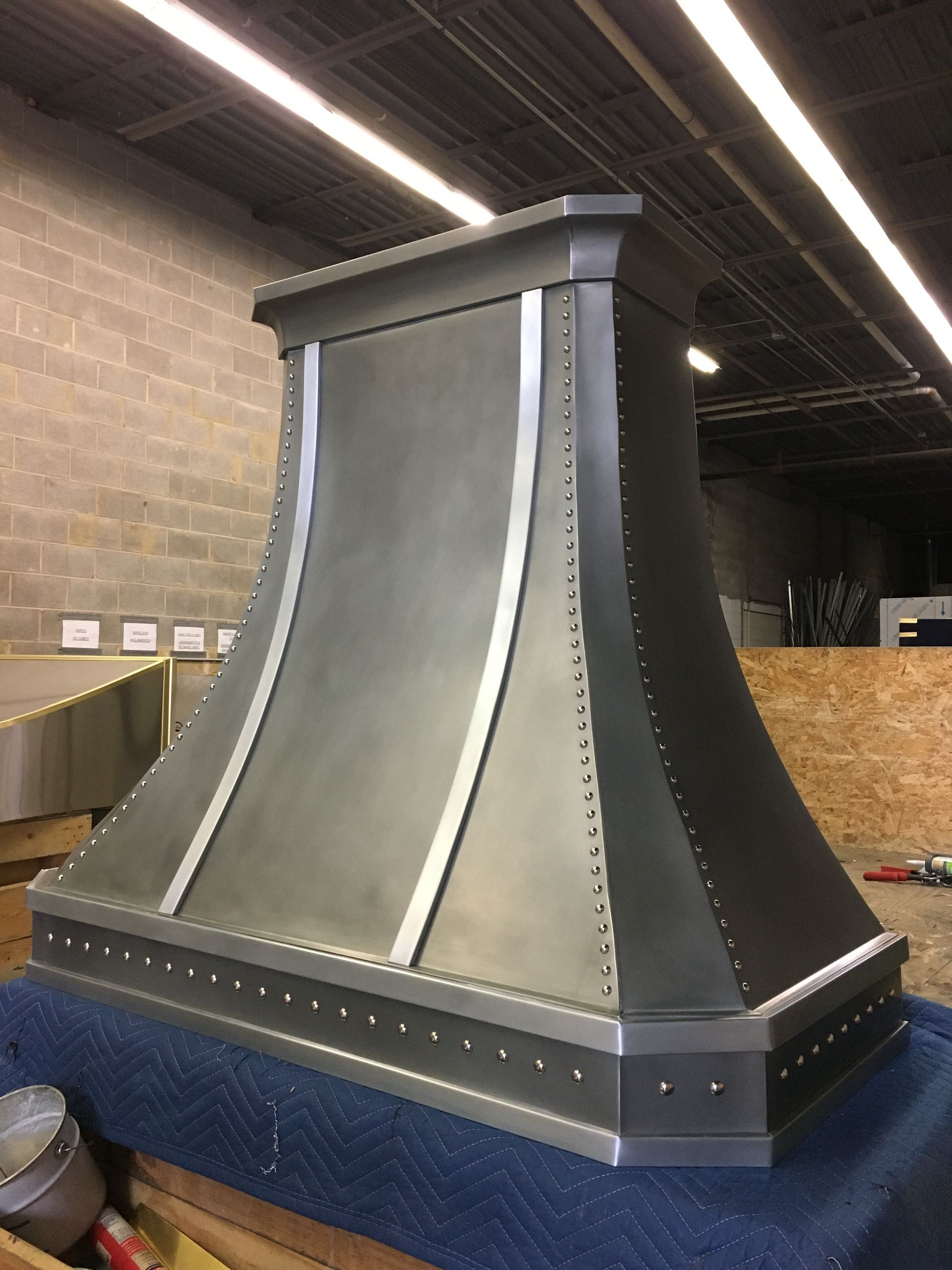 Large gray decorative vent or chimney cap with riveted black base in an industrial workshop