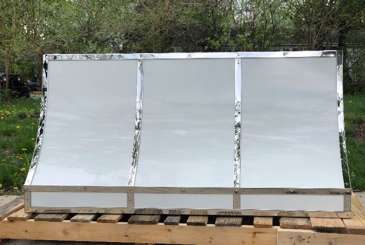 Three silver solar panels mounted on a wooden pallet outdoors.