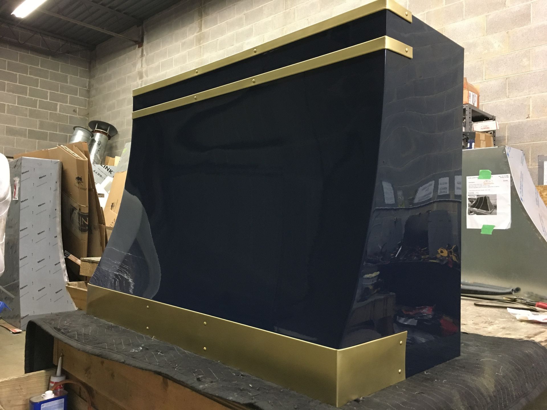 Large black-and-gold machine or kiosk in a workshop with unfinished equipment around it.