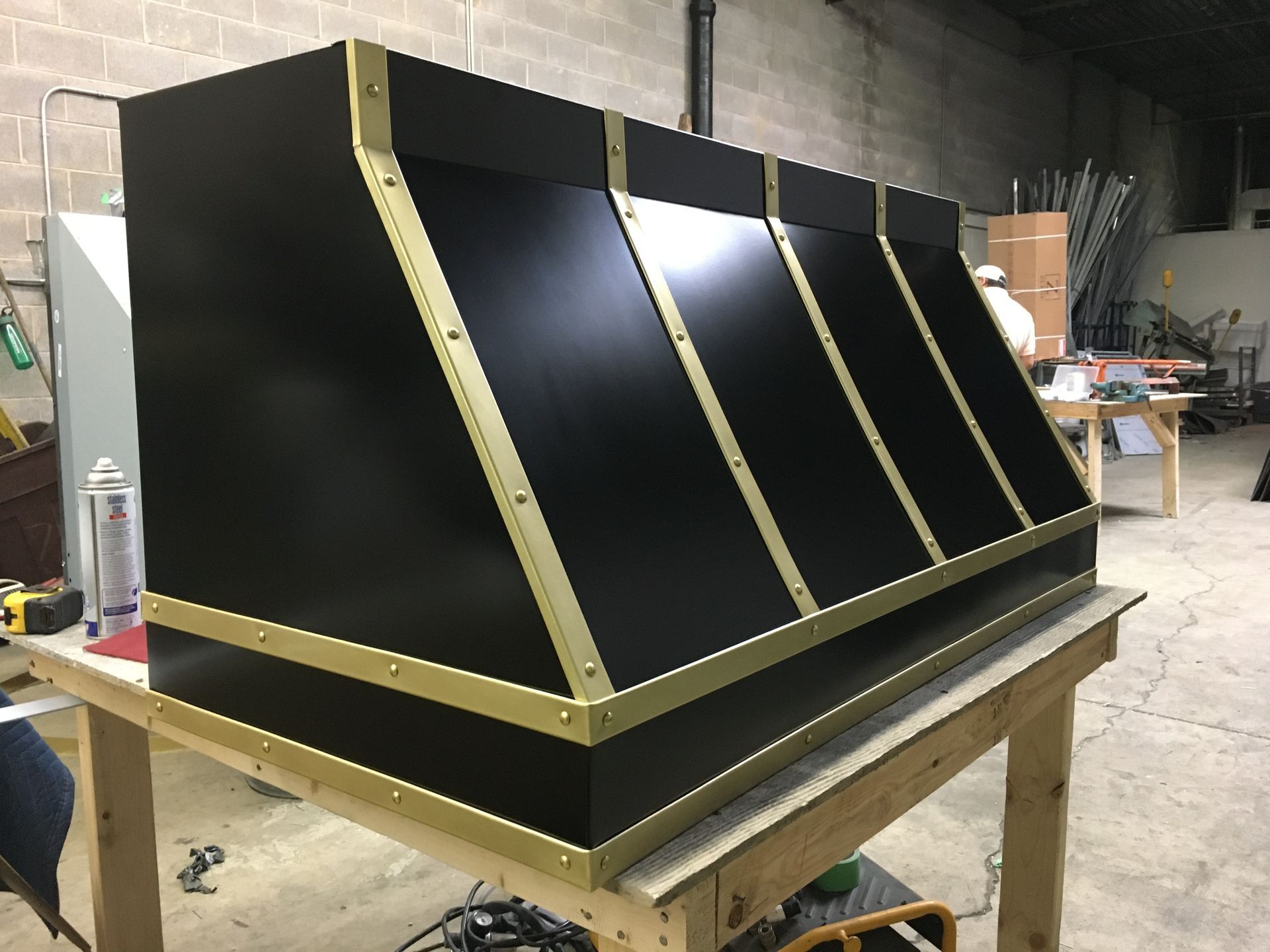 Black angled metal housing with gold trim on a workbench in a workshop.