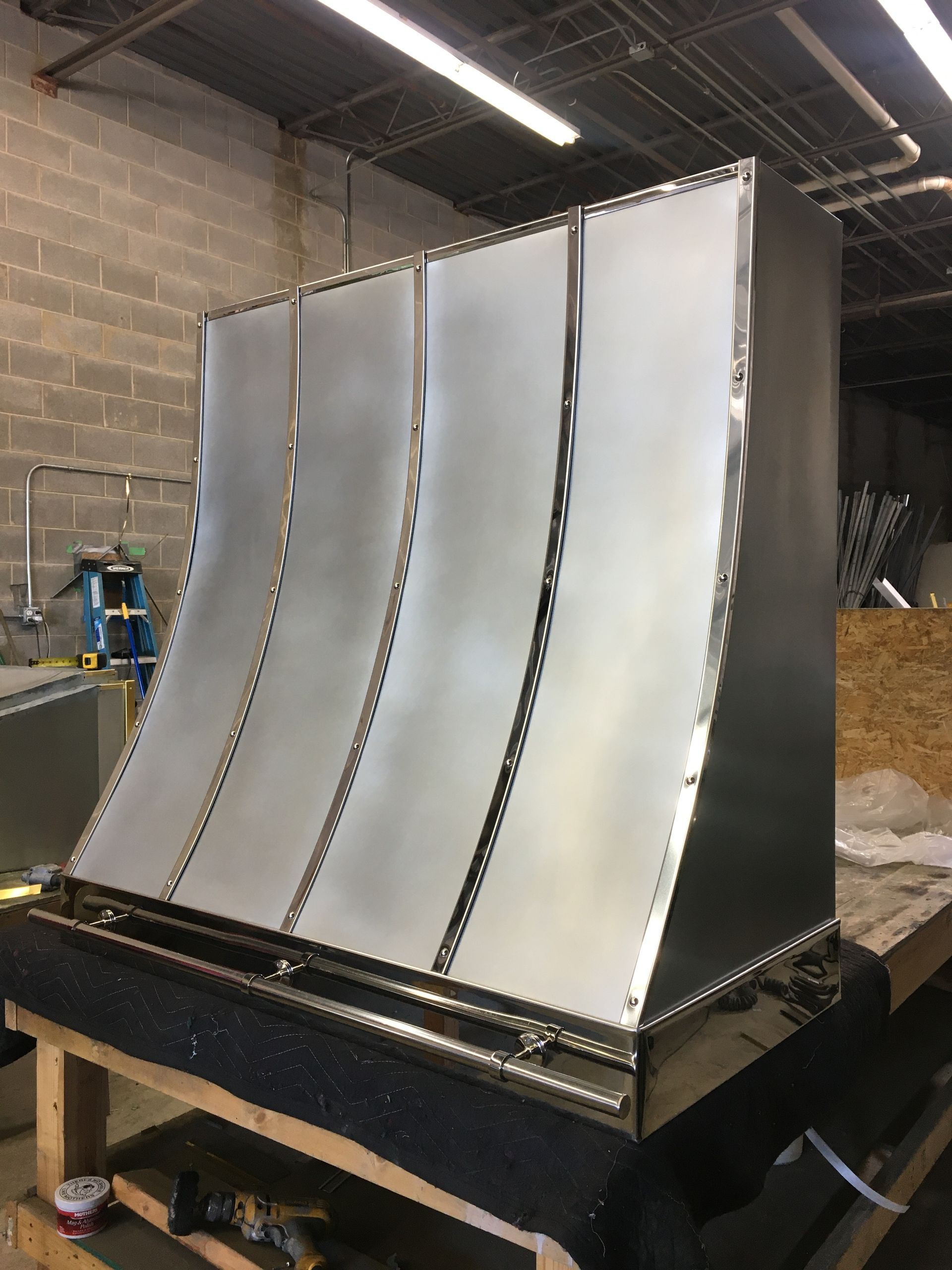 Large curved metal panel assembly in a workshop, with silver sheets mounted on a black base.