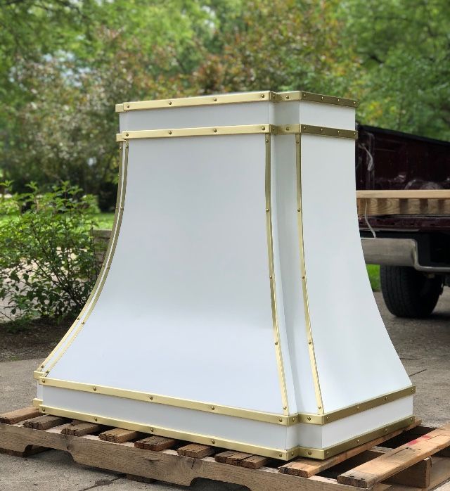 White decorative chimney-style structure on a wooden pallet outdoors, with gold trim and trees in the background