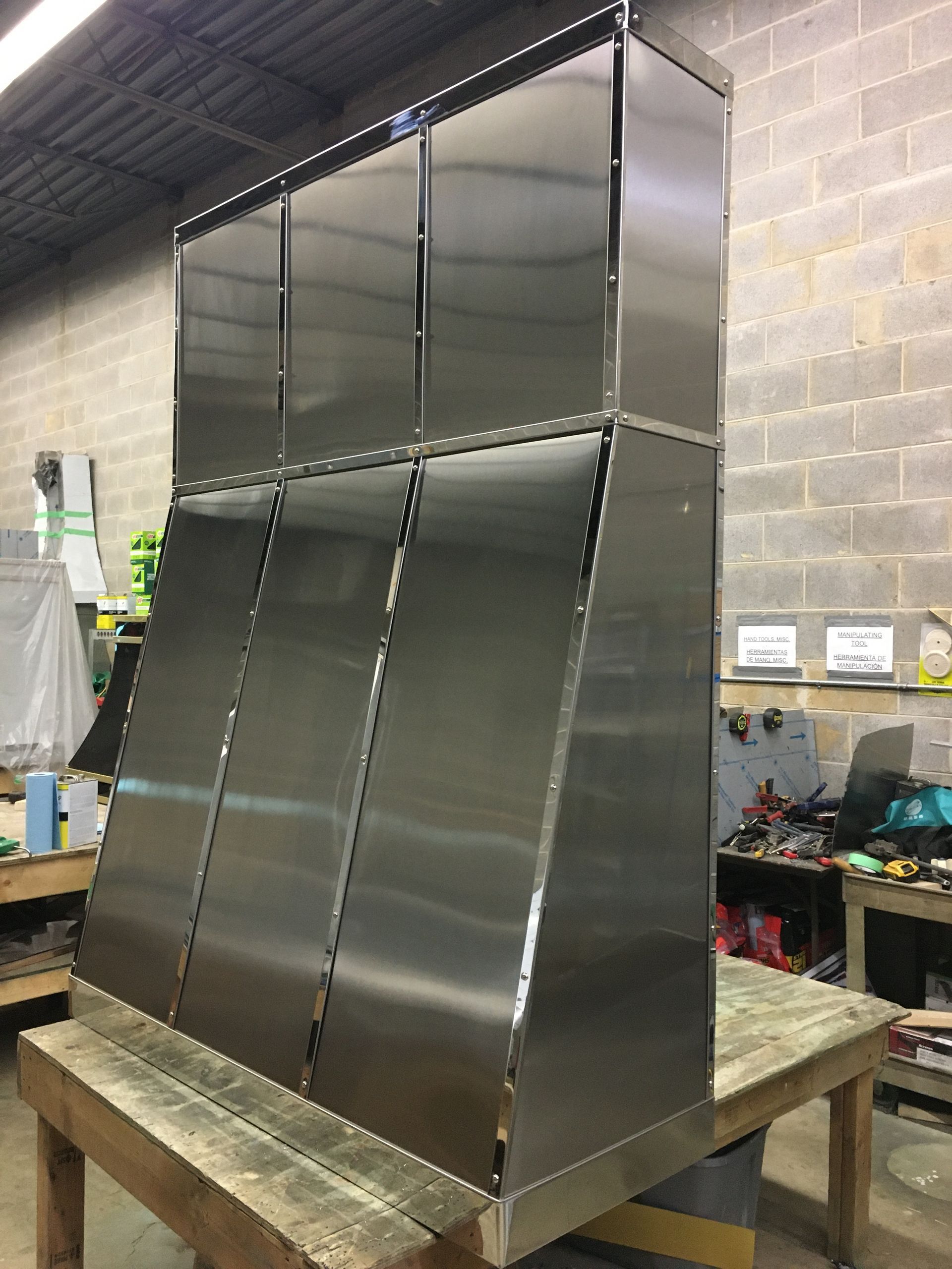 Stainless steel industrial metal hood or duct assembly on a workbench in a workshop