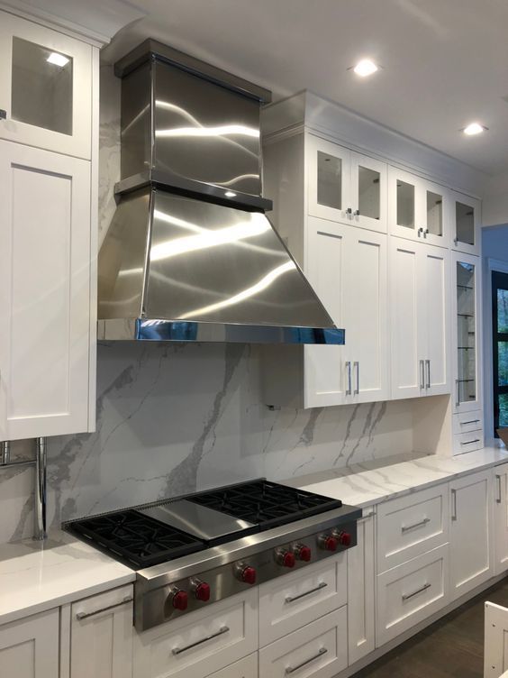Modern white kitchen with stainless steel range hood, gas stove, marble backsplash, and cabinets