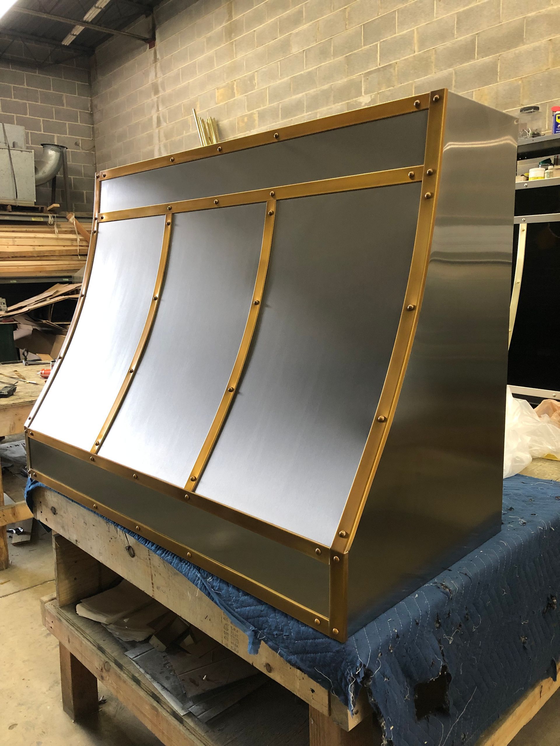 Metallic curved panel with gold trim displayed on a workshop bench in an industrial setting