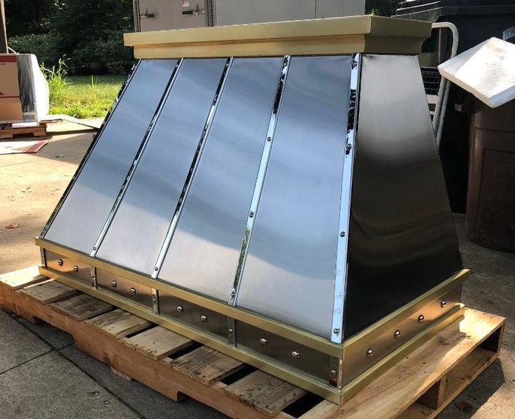 Metal rooftop vent or HVAC housing with reflective silver panels, sitting on a wooden pallet outdoors.