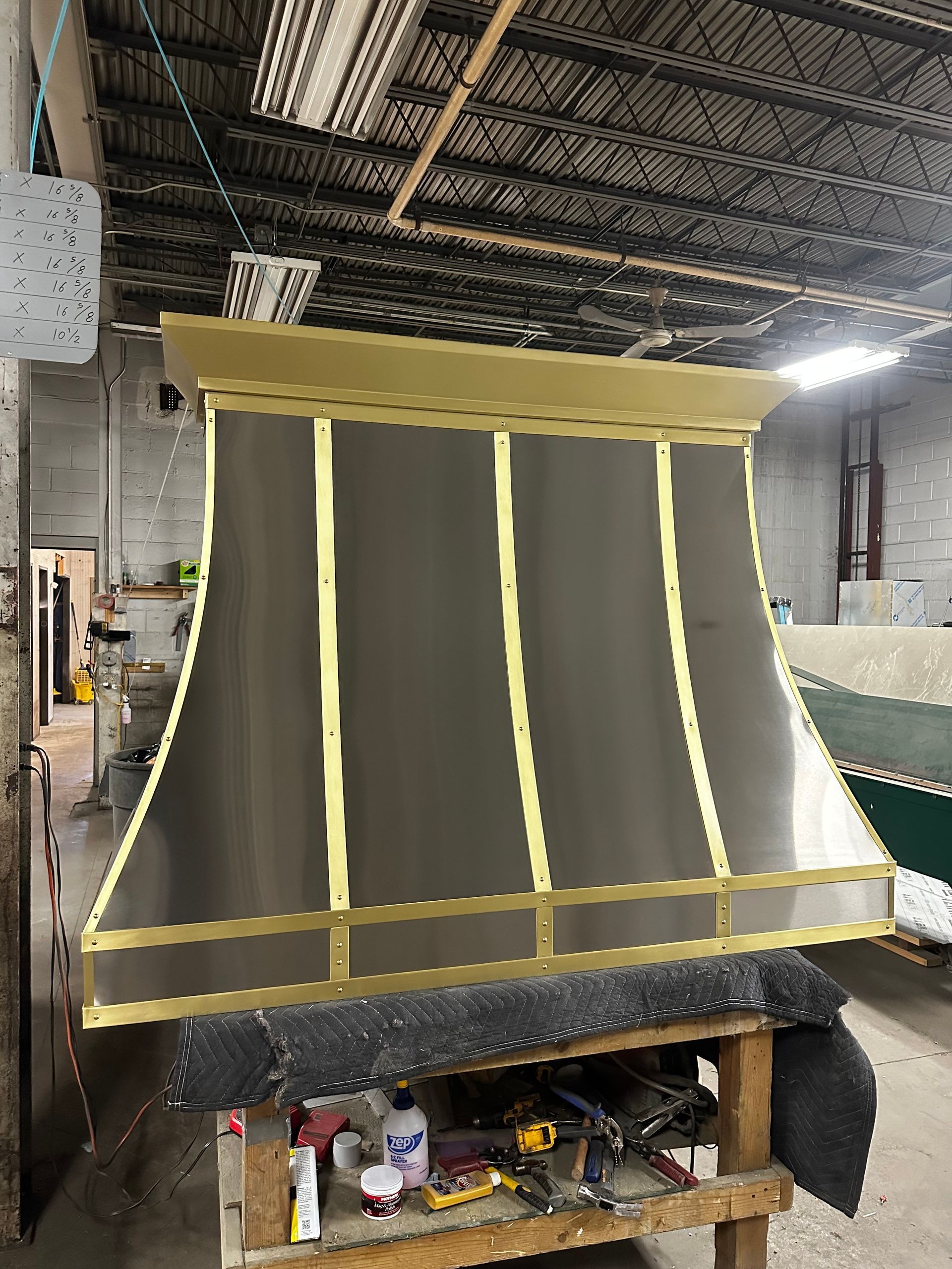 Large black-and-yellow industrial exhaust hood in a workshop, with tools and supplies stored underneath.