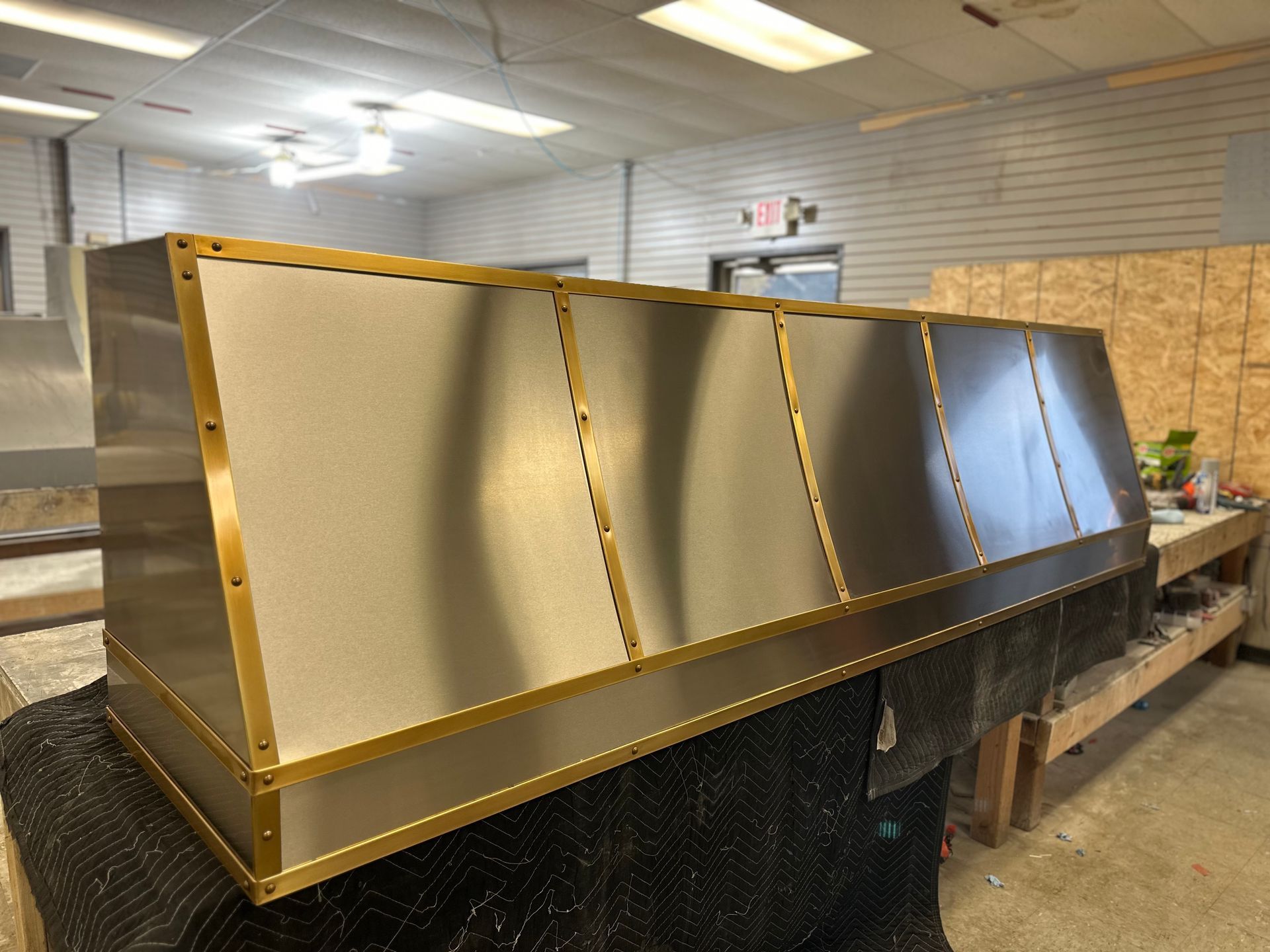 Large gold-framed metal display panels in a workshop, with a black base and workshop tables behind them
